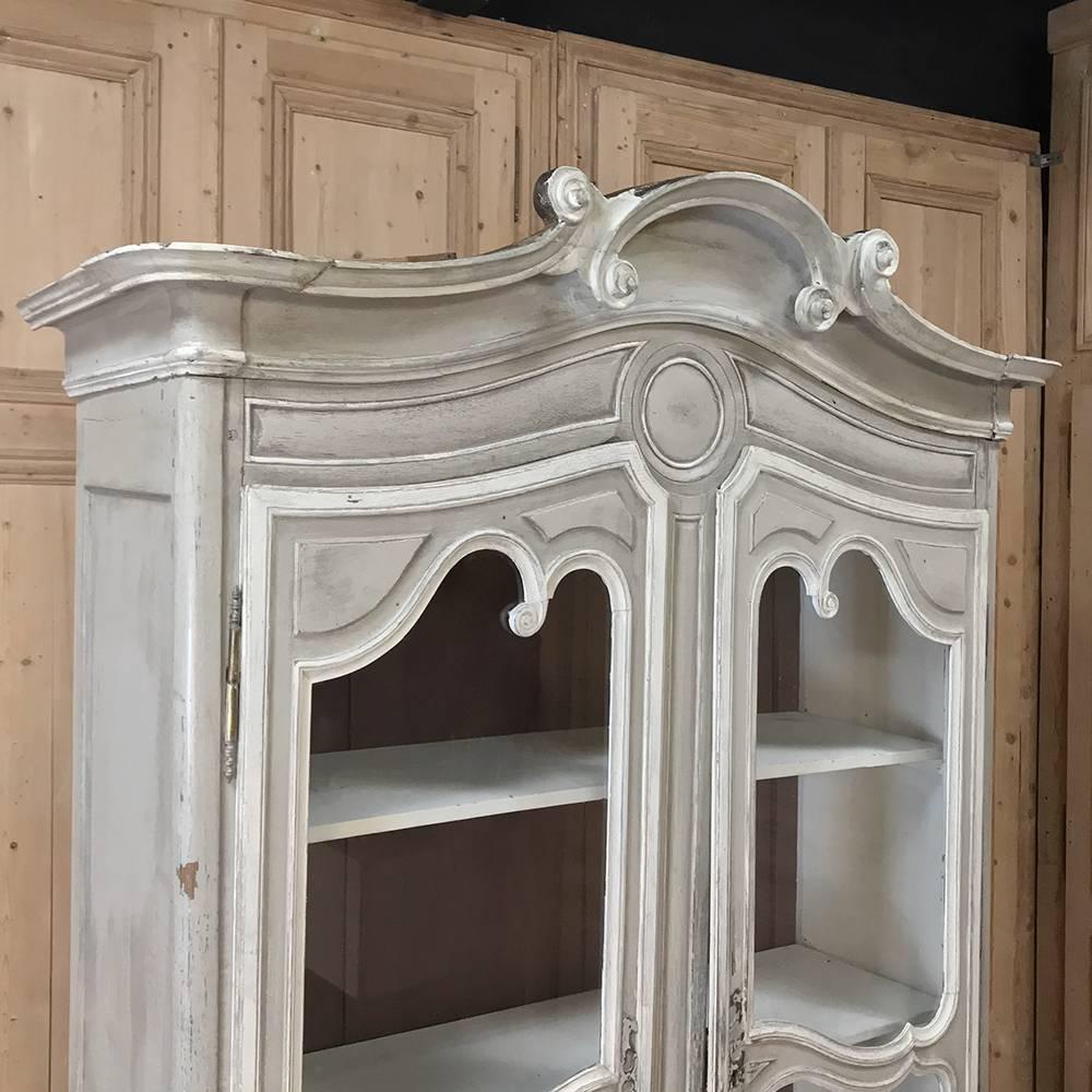 19th century Country French whitewashed Louis Philippe bookcase or vitrine is the perfect piece to display and store your family's finest! Bold, arched crown presides over scrolled doors both on the upper tier which are glazed to allow viewing the
