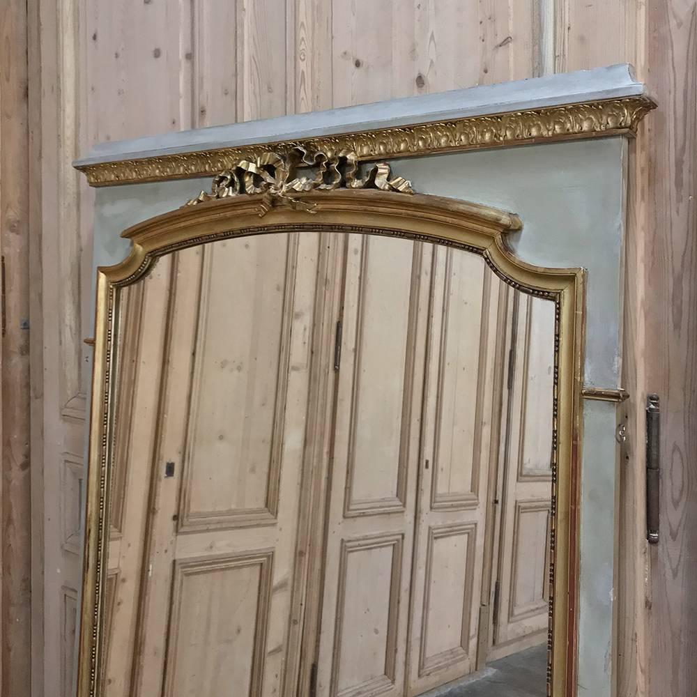 19th century French Louis XVI gilded and painted mirror features a ribbon motif on the crown of the generously sized glazing with gold highlighting on the carvings and molding complementing the patinated painted finish. Perfect for creating a focal
