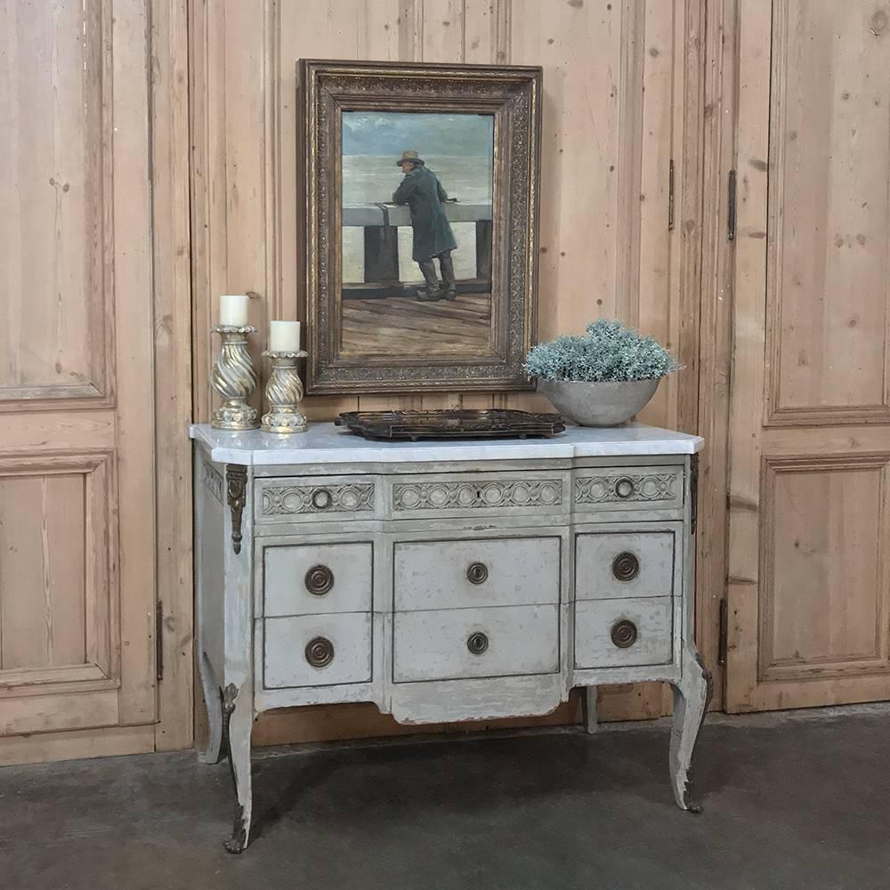 19th century French Louis XVI painted marble-top commode features a lovely distressed painted finish with brass bordering and bronze ormolu mounts from the shoulders of the legs to the drawer tier above, and is topped by contoured Carrara marble for