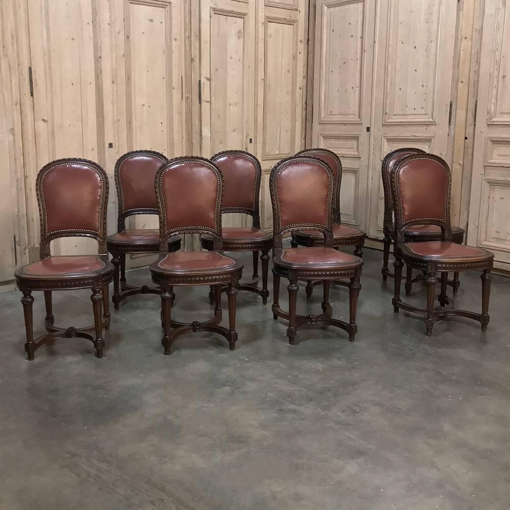 Set of eight antique French Louis XVI leather dining chairs feature hand-carved magnificence around the entire upper framework, with tapered and fluted legs below connected with double bowed stretchers for graceful support. Contoured and rounded