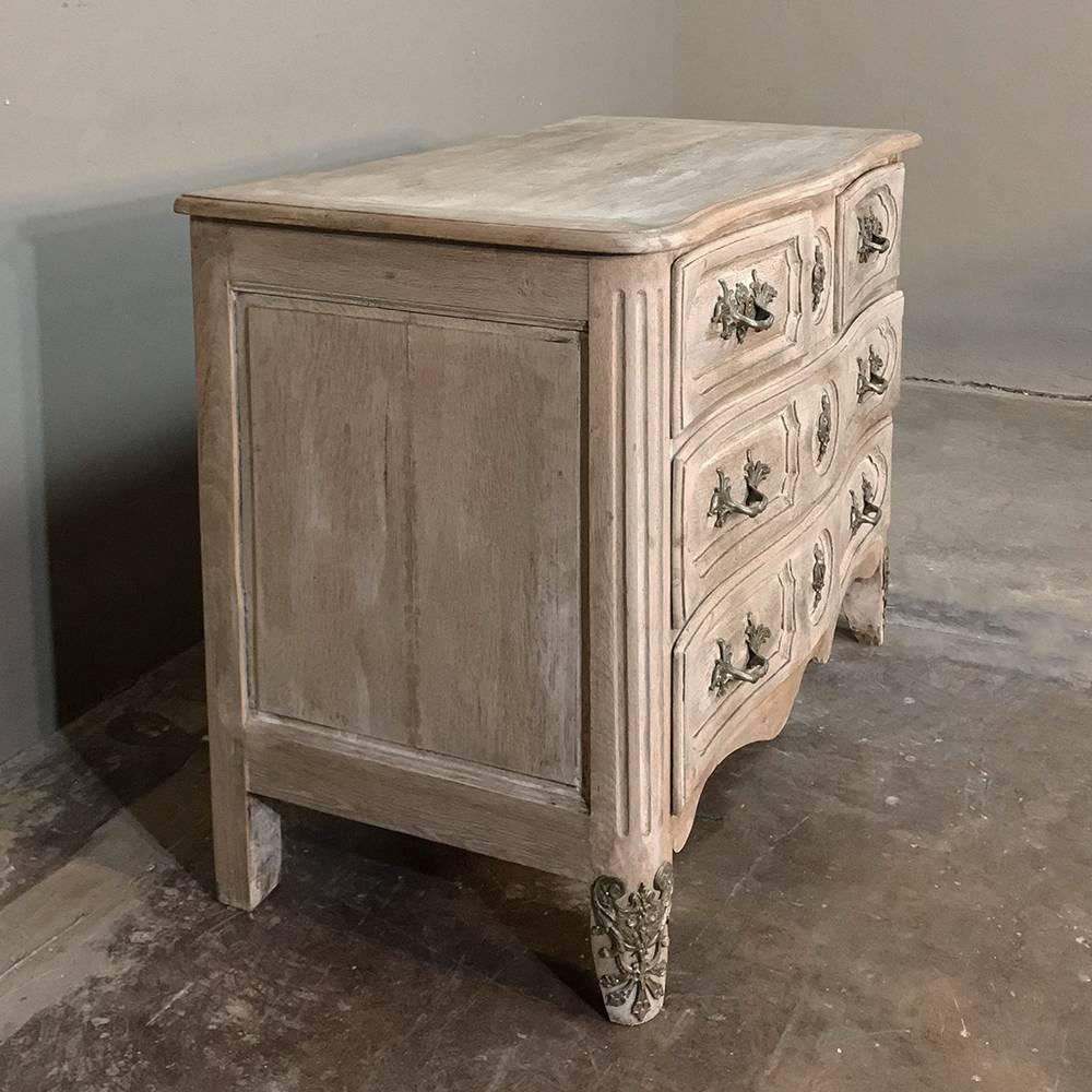 18th century Country French Louis XIV stripped oak commode will command the attention of all who enter the room, with exceptional lines including bowed front and chamfered drawer facades, luxuriously enhanced by exquisite jewelry-quality cast bronze