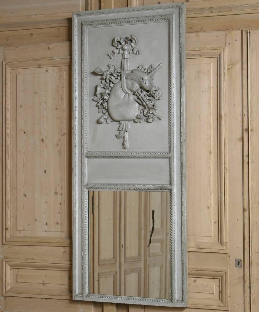 Country French painted trumeau, 1890. Gorgeous antique Louis XVI style trumeau mirror in a weathered grey with original paint finish. Delicate hand-carved floral, ribbon and bagpipe detail at top with a lovely romantic shapes. Original mirror glass