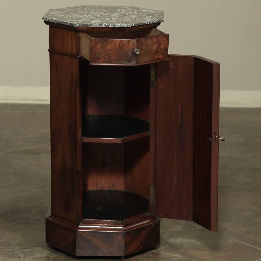 Handcrafted from mahogany during the Louis Philippe Period, this unusual marble-top antique furniture can serve as a pedestal, an end table, or a nightstand! Topped with marble, it features a drawer with two facets to follow the casework, and a