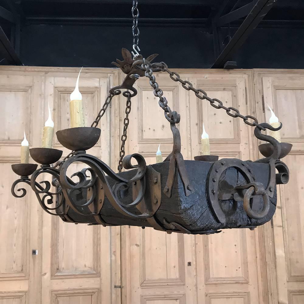 Antique country French wood and wrought iron chandelier combines the rustic authenticity of an old oak beam with the hand-forged wrought iron scrollwork of a master blacksmith, who even put one of his products, a horseshoe, on display on each end!