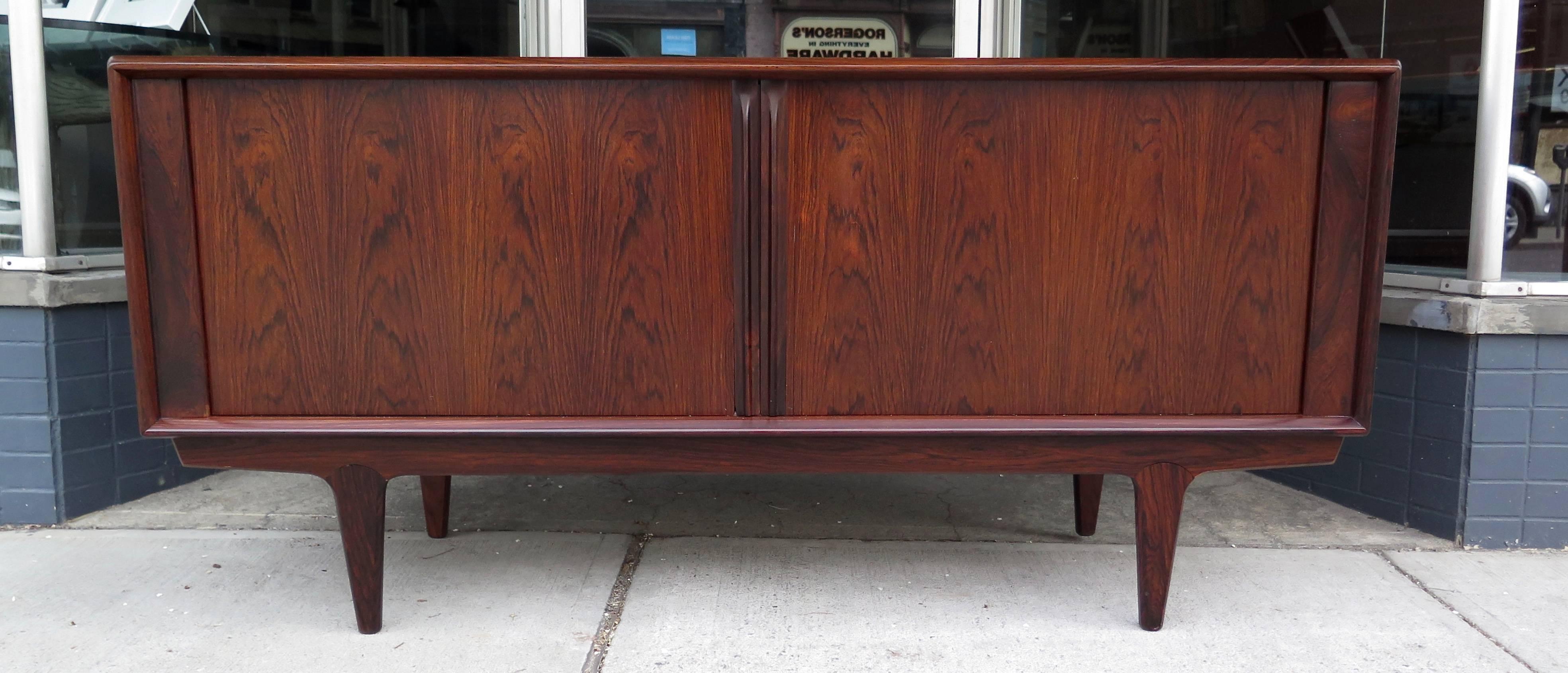 Made in Denmark. Restored. Really great rosewood grain patterns. Inside has three shelves and three small pull-out drawers. Tambour doors work smoothly. Few veneer lines on top. One small little chip on front left door, at very bottom, near the