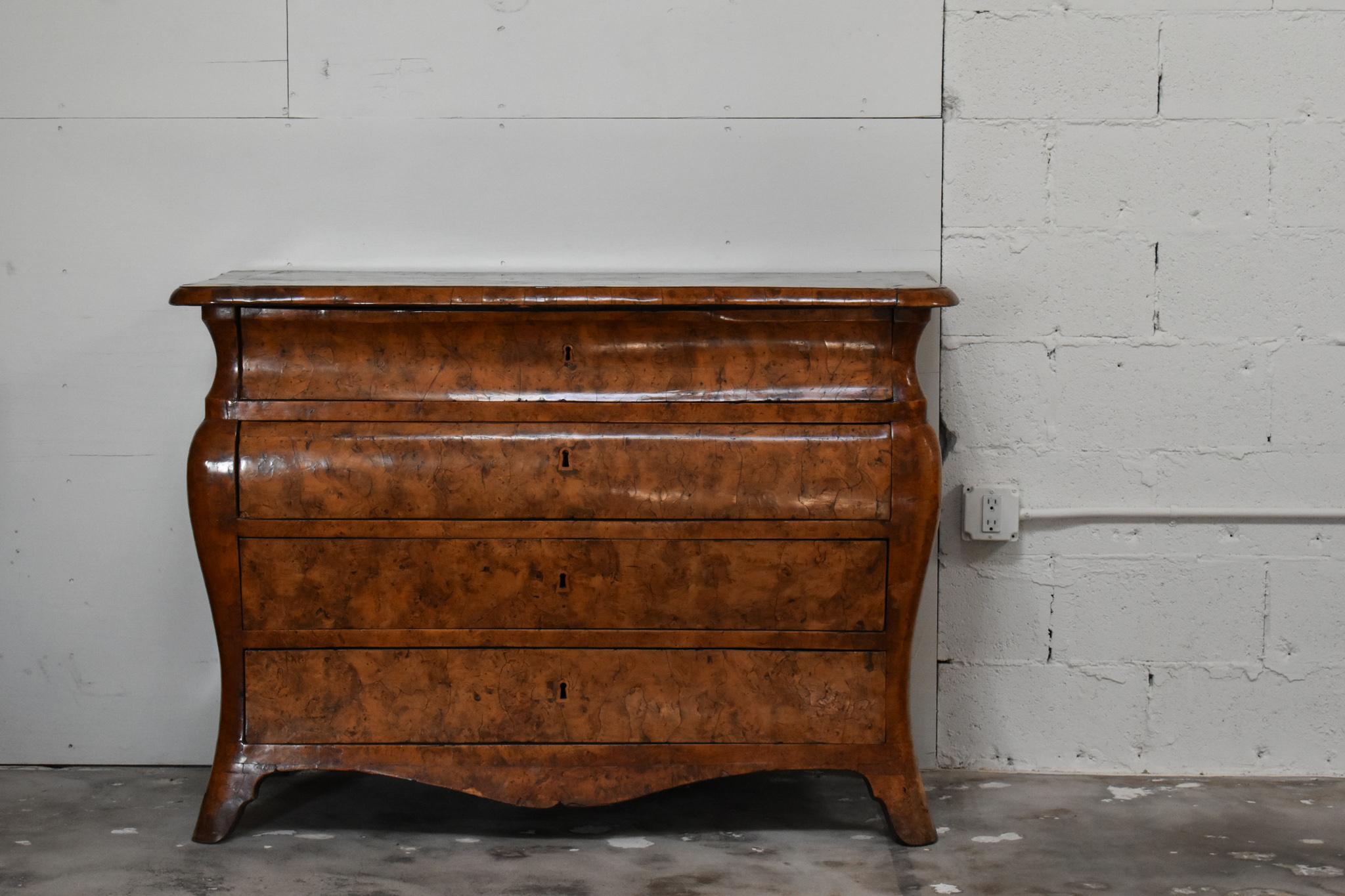 This exquisite chest showcases the iconic curvaceous bombe silhouette, typical of Italian craftsmanship during the period. Crafted from rich burlwood, the surface displays mesmerizing grain patterns and a lustrous patina developed over time. The