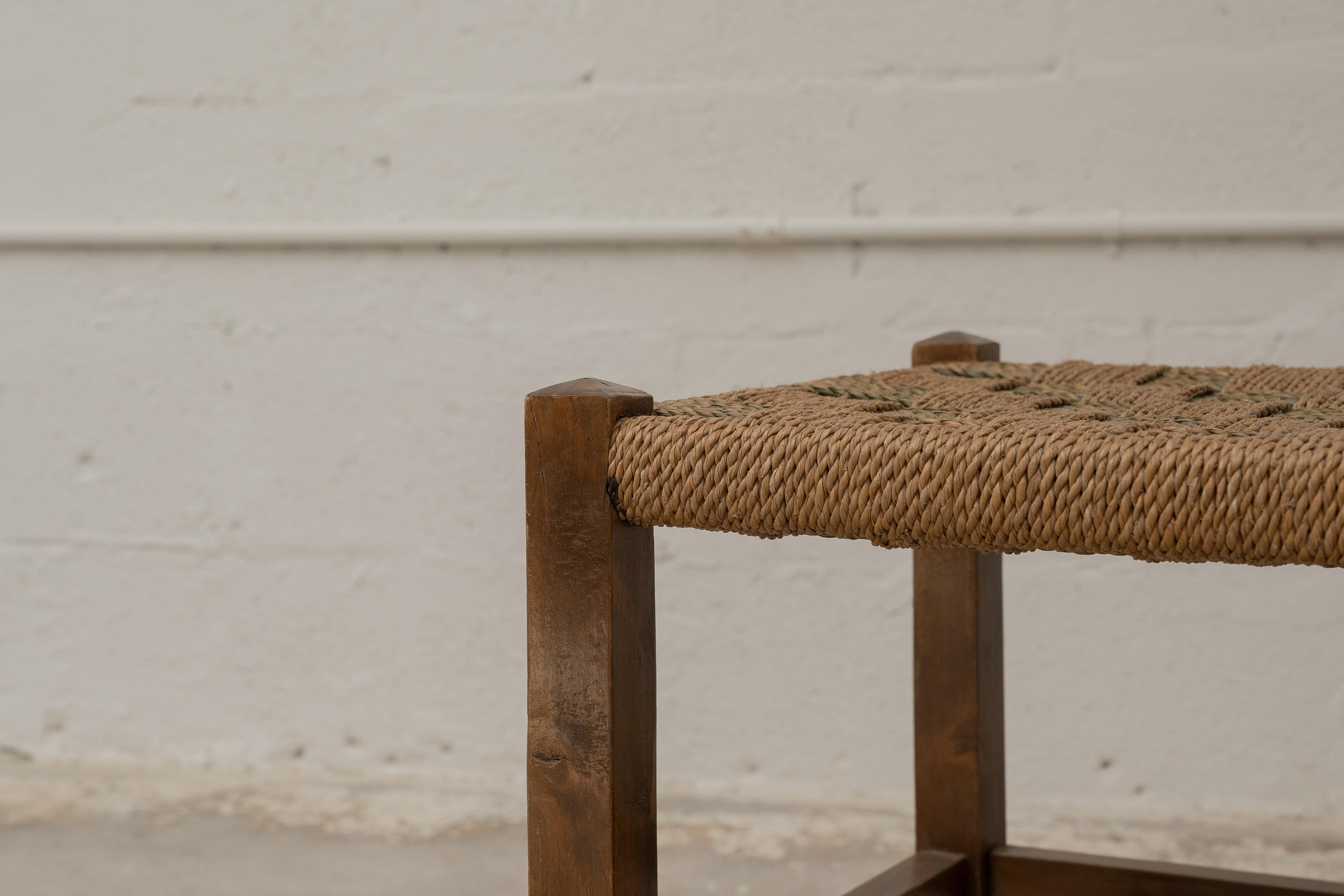 A charming stool dating back to the 1920s, showcasing the craftsmanship and honest materials of that era. The sturdy wooden frames are complemented by hand-woven seagrass seats, arranged in a distinctive checkerboard pattern that highlights their