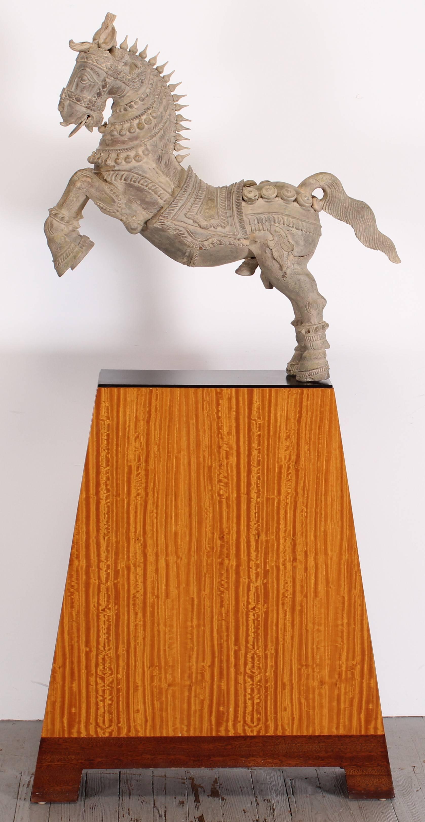 This carved wood horse has typical characteristics of vahana wood carvings made in India. It was probably made in the late 20th century, to replicate a much older piece. The horse sculpture, the metal base plate and the pedestal, separate to