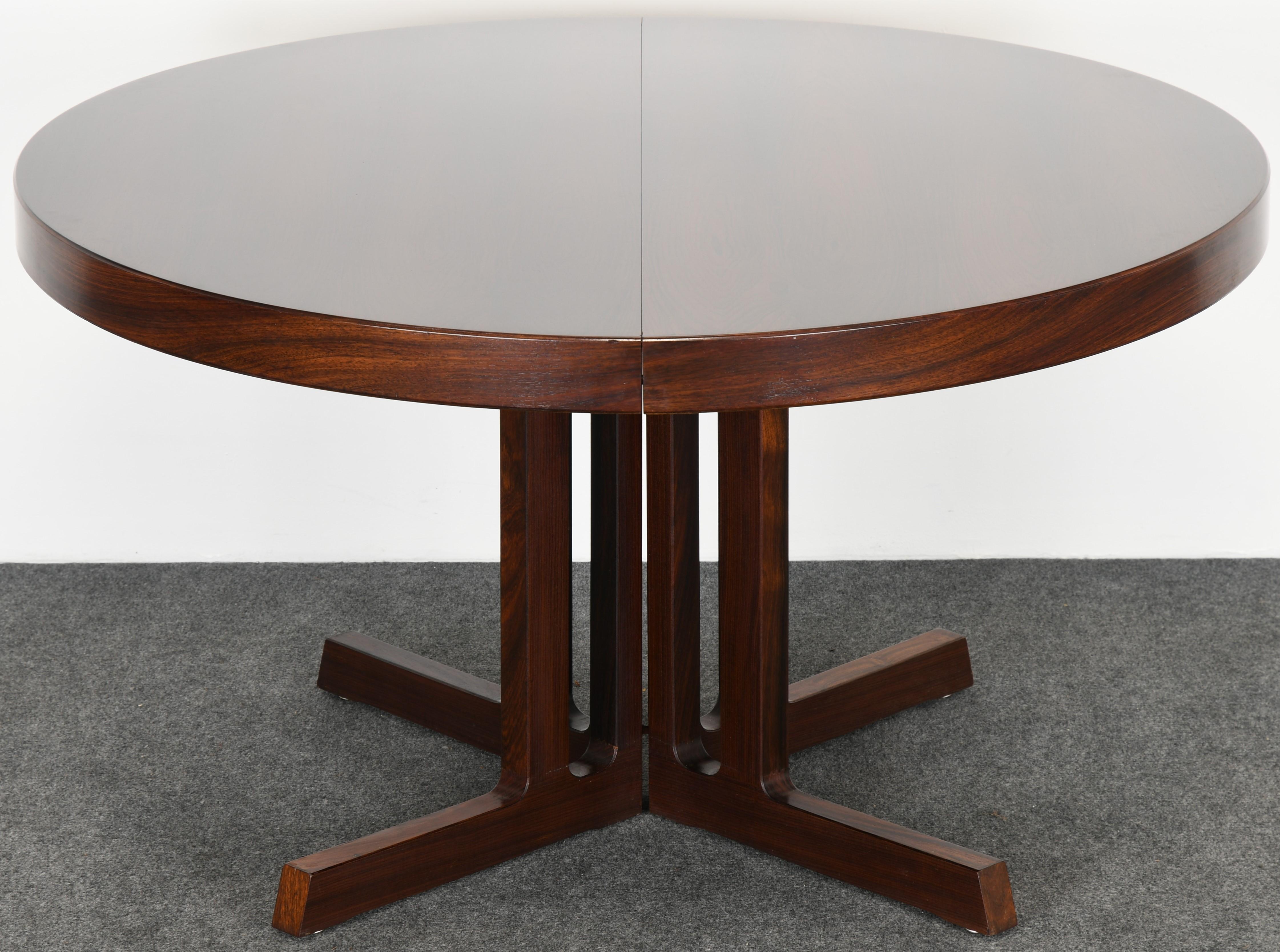 A functional Danish rosewood Mid-Century Modern Scandinavian Modern dining table designed by Johannes Andersen. The table has a beautiful rosewood grain, stately cross base with three leaves. It is structurally sound and in good