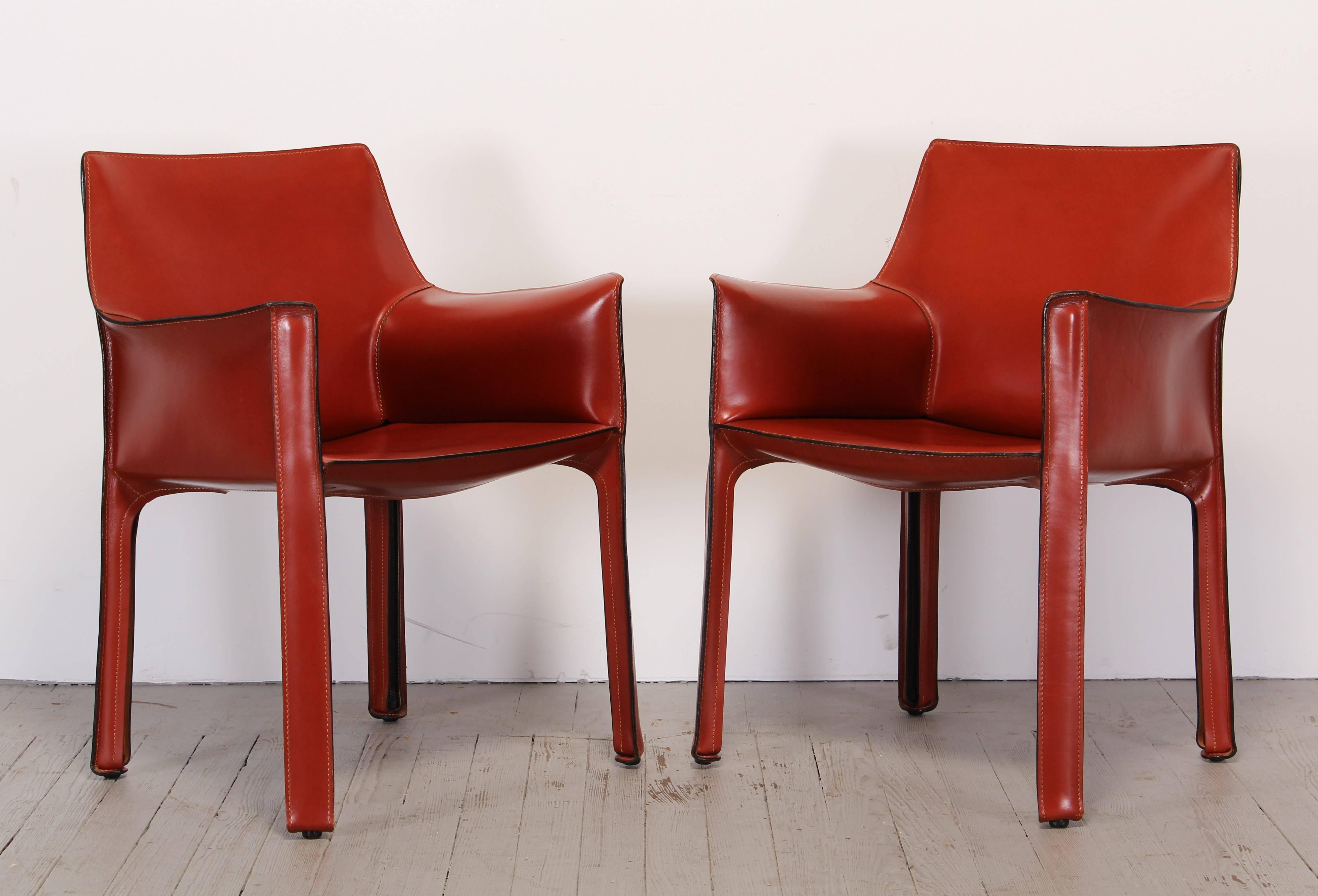 An orange-red leather pair of 413 cab chairs by Mario Bellini. The seat is padded with polyurethane foam under an enamelled steel frame. Leather upholstery zippered over the frame. The chair is now part of the permanent collection at the New York