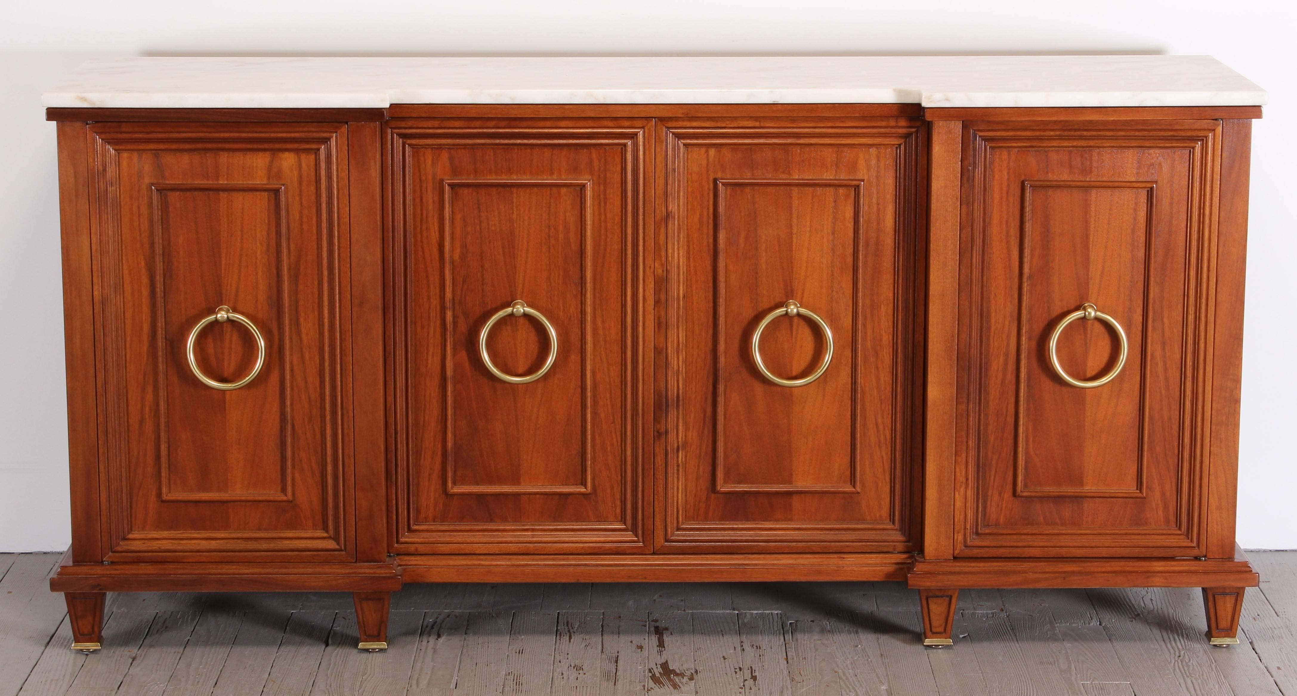 A wonderful walnut sideboard or credenza with four doors and four fabulous brass handles across the front. Cabinet opens to drawers, shelving and open storage. Done in the Hollywood Regency style with honed Carrara marble top.
