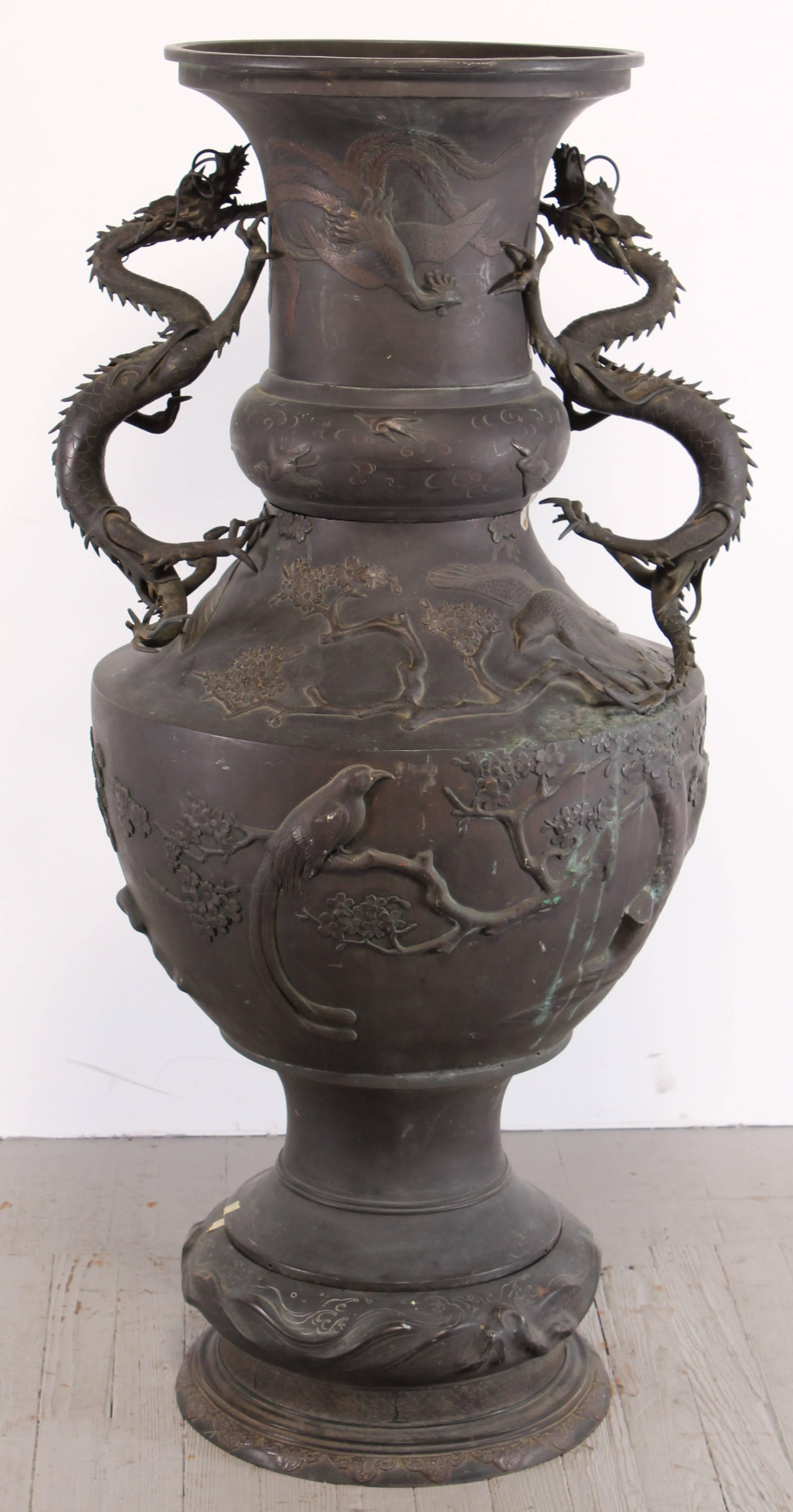 Vase monumental japonais en bronze avec deux grandes poignées en forme de dragon. Il semble y avoir trois oiseaux différents embossés sur la surface:: paon:: aigle:: grues. Date de la période Meiji. Les broches qui fixent les dragons au corps ont