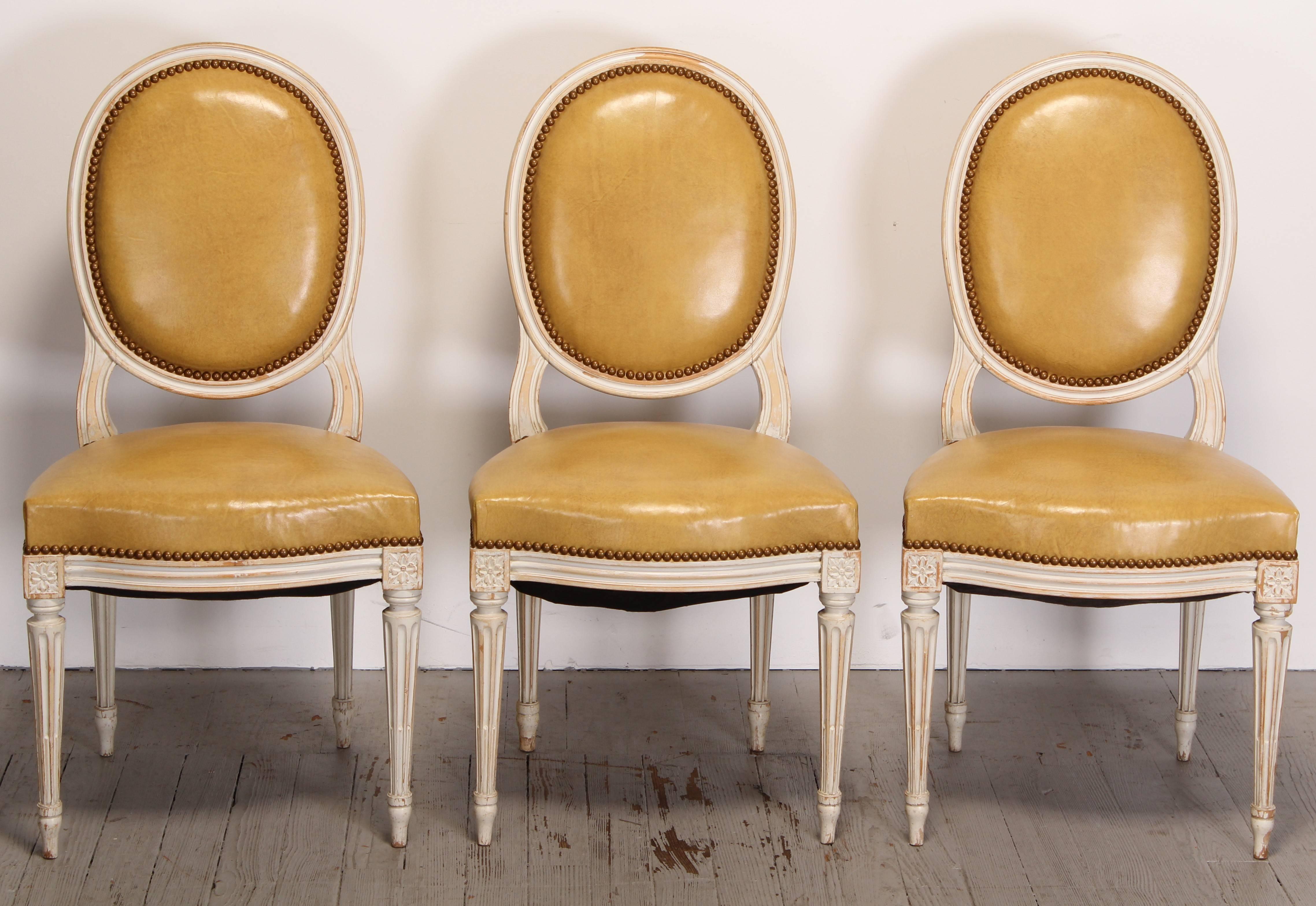 Set of six Louis XVI style painted beech dining chairs, upholstered in leather. All chairs except one are structurally sound, one chair the back rest has a slight wiggle. Several chairs the tied springs probably need to be redone. Both issues are an