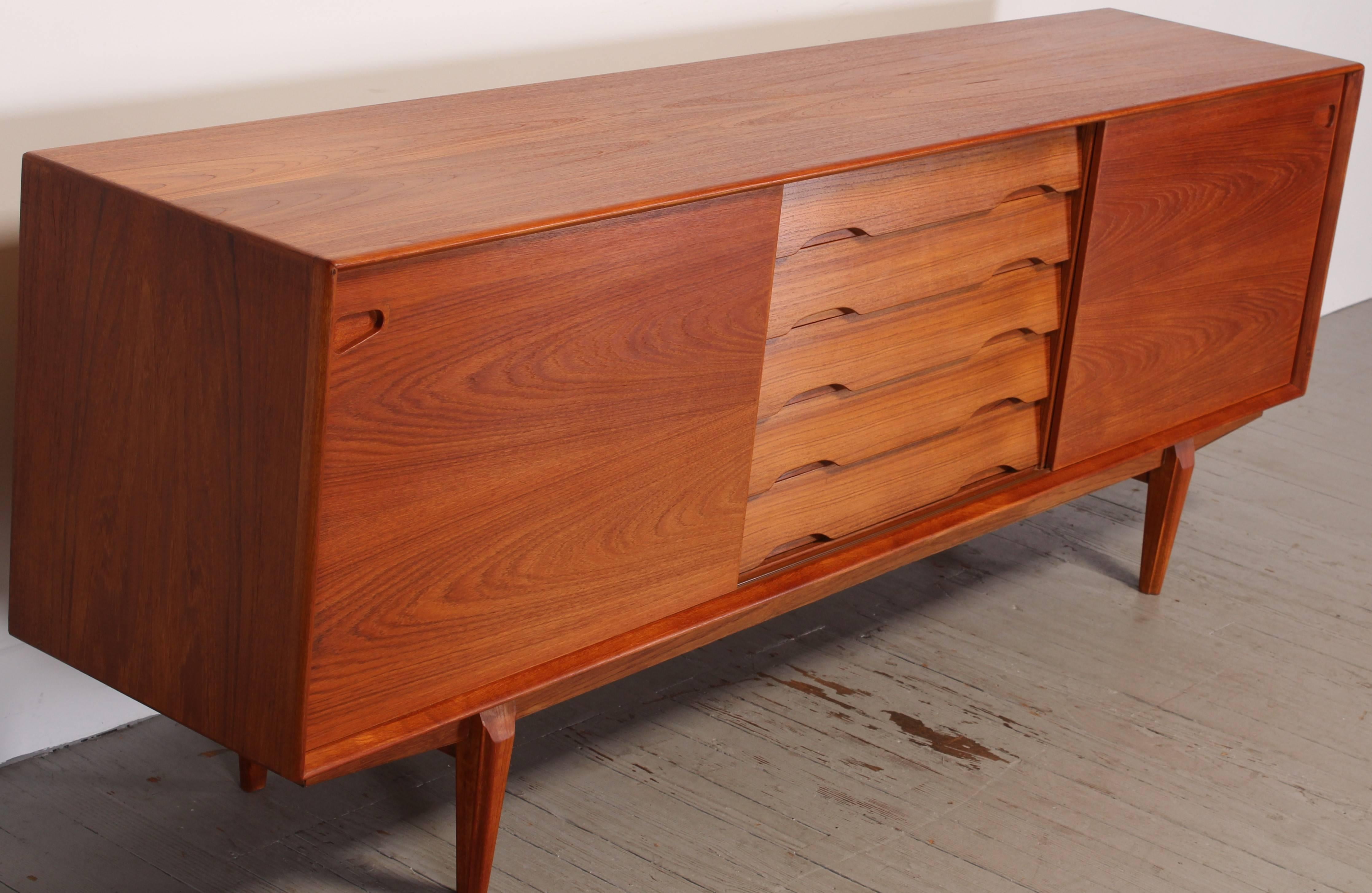 Teak credenza made by Dyrlund of Denmark. Two sliding doors and five drawers, top drawer has green felt lining. Adjustable shelves, use none or adjust the three included shelves as needed. Dyrlund label affixed inside cabinet.