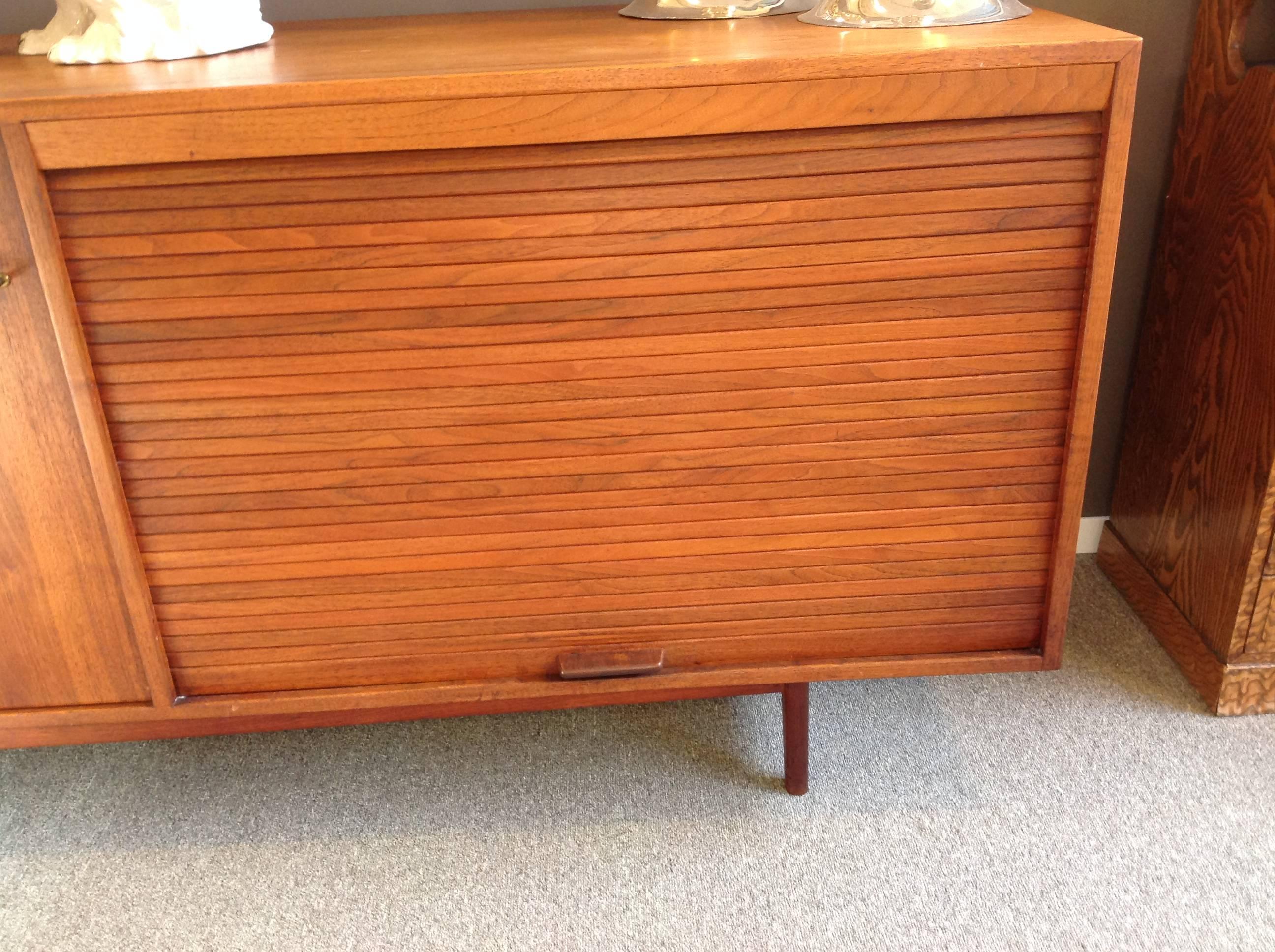 Modern teak credenza by Jens Risom (Danish American, 1916-2016) in two sections with two tambour doors, one teak and one plastic. The sections are movable and rest on the original wood frame. There is a shelf in the right cabinet that slides out for