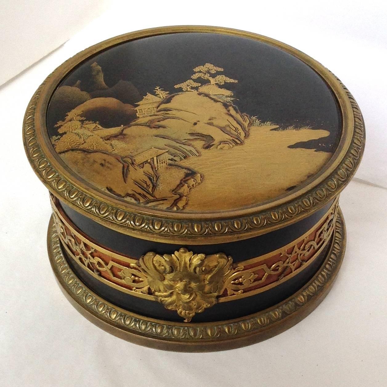 Antique French bronze box with early Japanese lacquer top depicting a seaside village. The lacquered top is early 19th century. The base is signed Bointaburet A Paris 52763 17. The sides have an openwork band with lion mask over a tan veneer. It