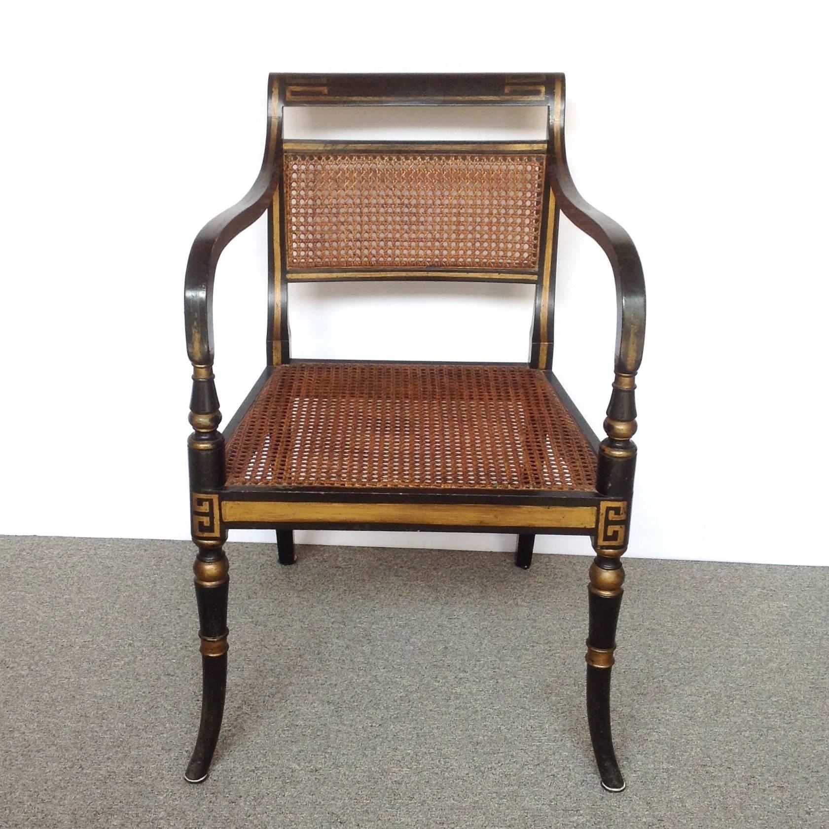 Pair of English Regency black and gilt painted wood open armchairs with cane seats and back. Gilt outlines and Greek key decoration on the front legs, 
circa 1830.