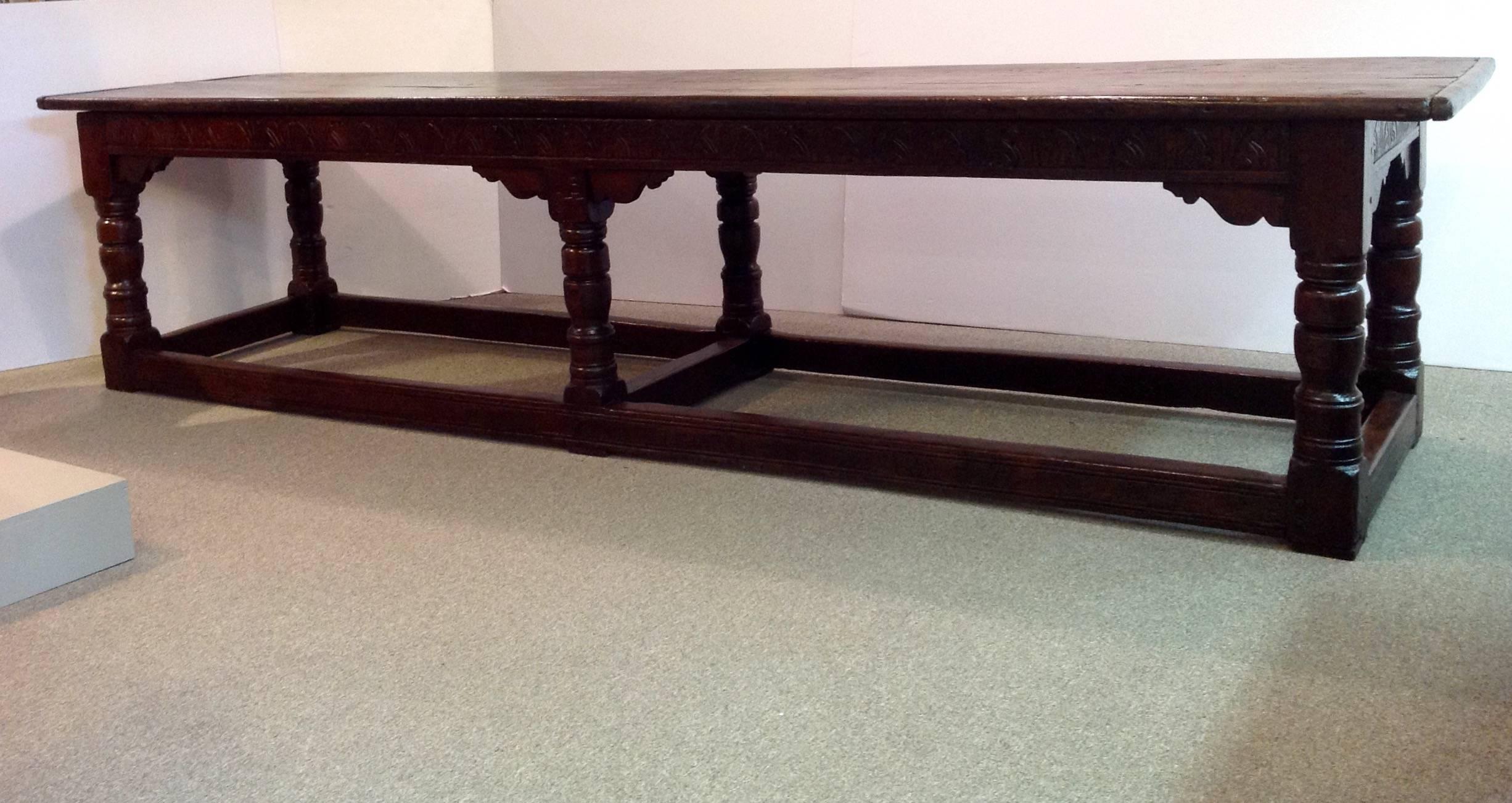 Antique long English oak serving or refectory table with a two board top on a stretcher base. The stretcher is carved on three sides with stylized tulips and the initials LB over 1677. It has an old patina. It dates from 17th century and later.