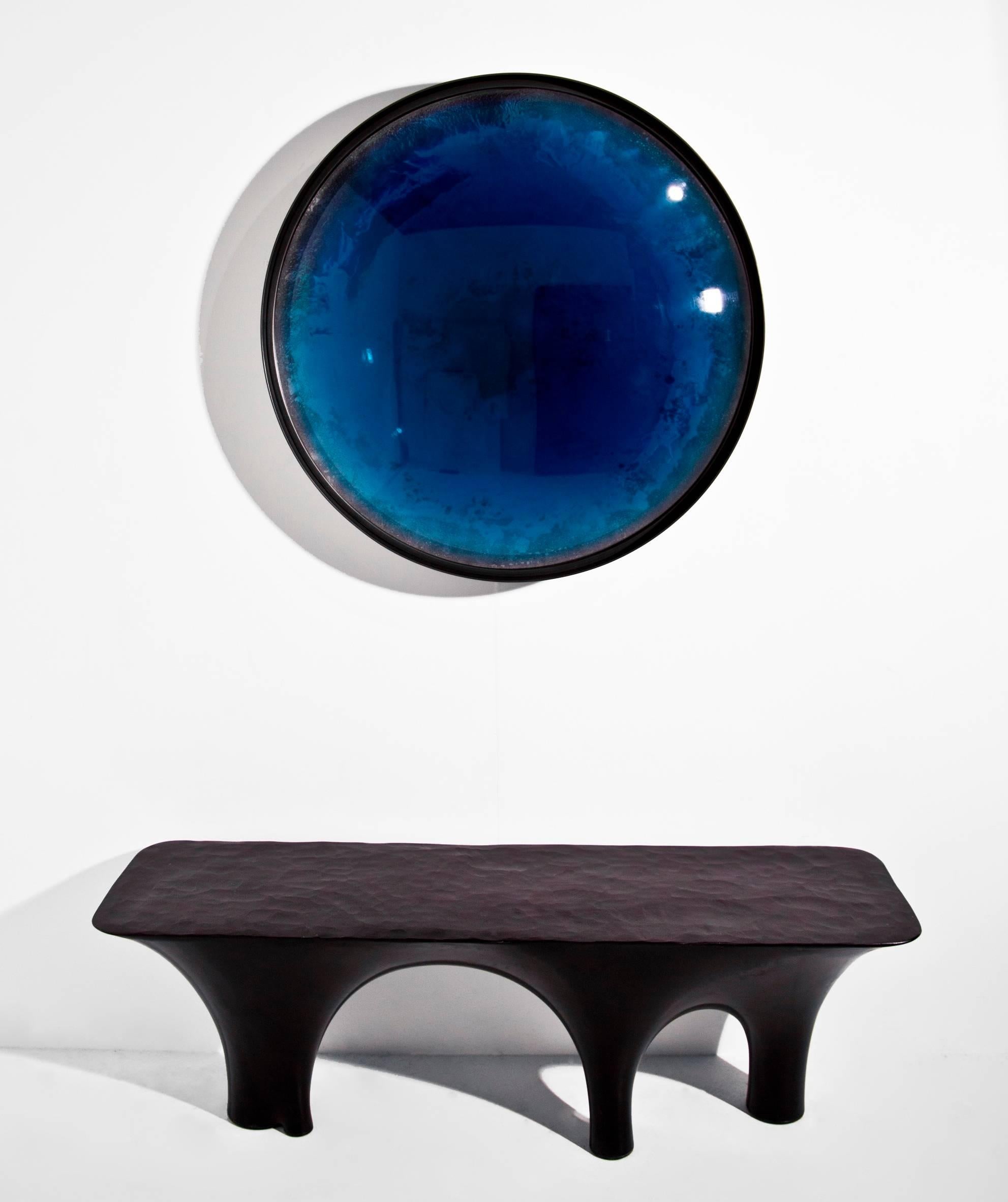 The Ionian Iris is unique on the market. It is a lens cast in translucent, cerulean blue tinted resin, layered over a hand silvered panel, set within a patinated steel frame. This creates a unique optical effect, magnifying and manipulating the