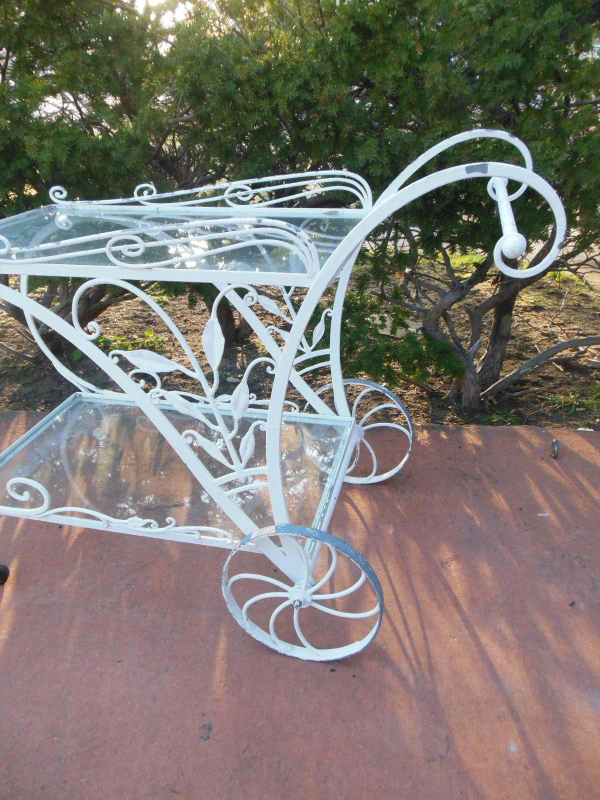 A wrought iron tea cart by Salterini with two glass shelves. The tea cart with
Salterini's typical details of leaves and curlicues. The front wheels are modern
replacements, and the cart maintains an old painted finish.
      