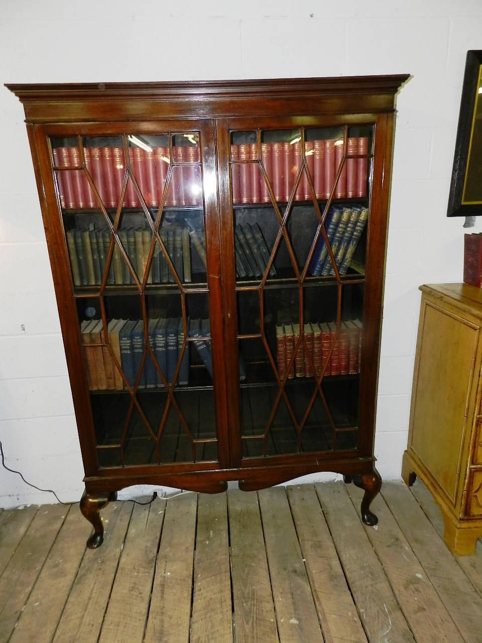 This is an English two-door astragal glazed bookcase on cabriole legs. Having three adjustable shelves, the piece is able to accommodate several sizes of books. A swept mahogany base adds a stylish accent to the bookcase.