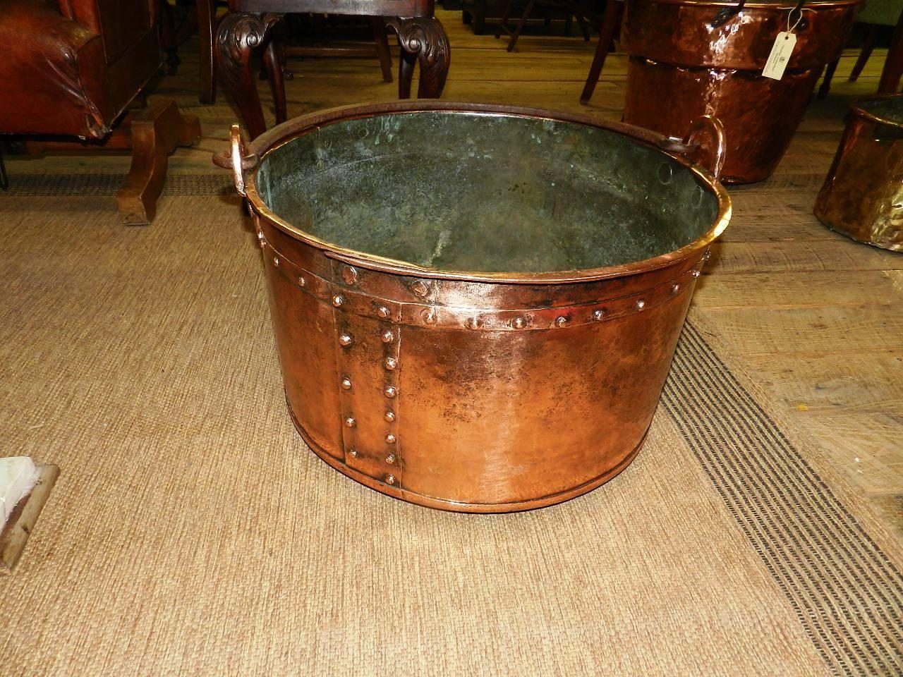 An antique copper cauldron from a French textile mill with wonderful character. The rivets and well worn appearance greatly enhance the piece. Superb for use as a fireside log holder or for drinks on the porch!