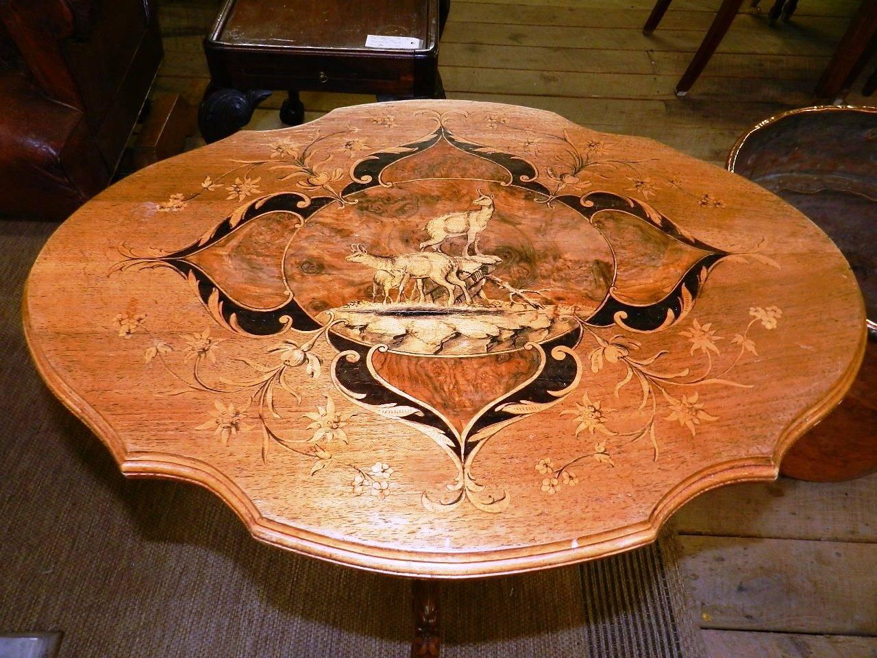 A signed antique walnut inlaid table from the Austrian Tyrol with a tilt top and carved three-legged pedestal base. The inlaid and decorated top also depicts two chamois.