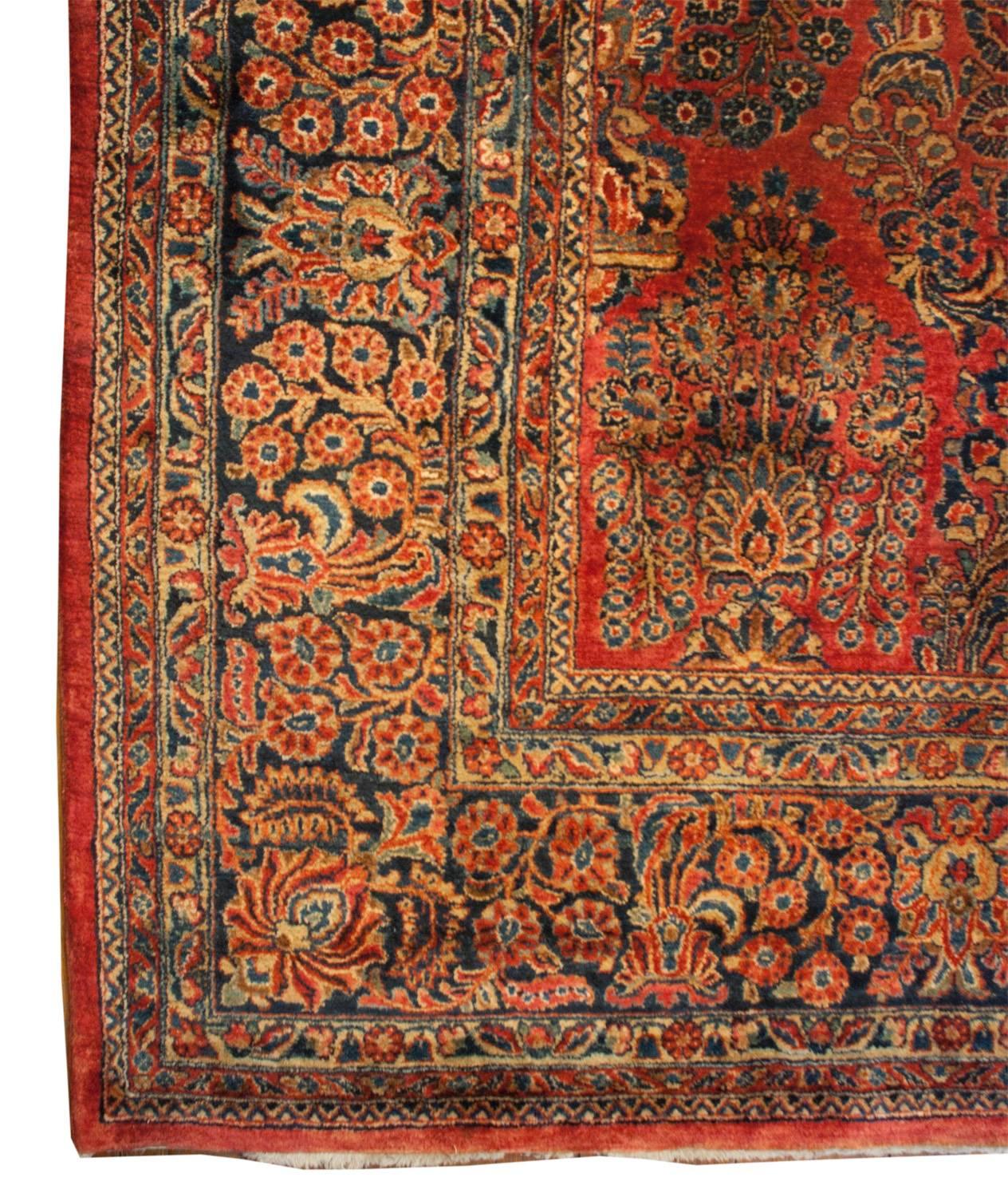 An early 20th century Persian Sarouk rug with an amazing all-over pattern of myriad flowering branches and trees woven in indigo and natural undyed wool, on a rich light cranberry background. The border is woven similarly in pattern to the field,