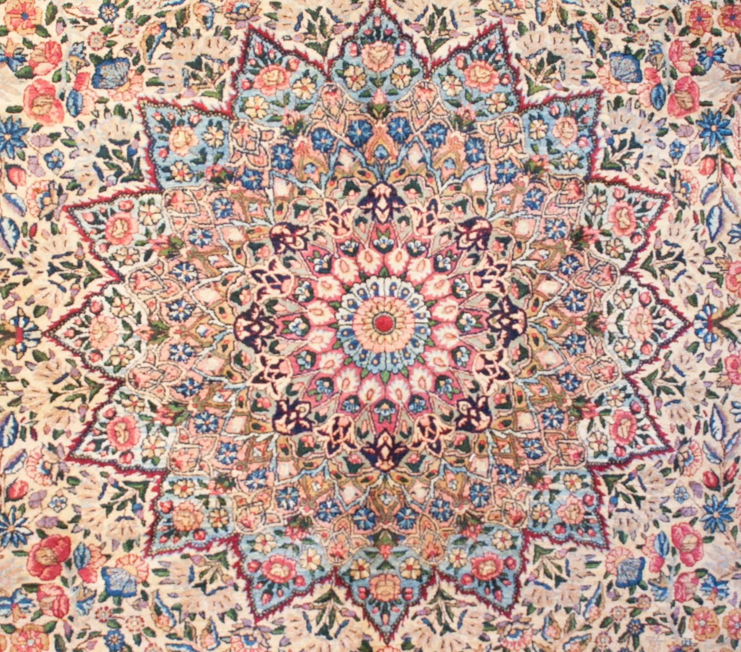 Un incredibile Kirman persiano dell'inizio del XX secolo con un elaboratissimo disegno multicolore di tralci di vite con una miriade di fiori su uno sfondo color crema. Il medaglione è il migliore che abbiamo visto! Come un caleidoscopio, il disegno