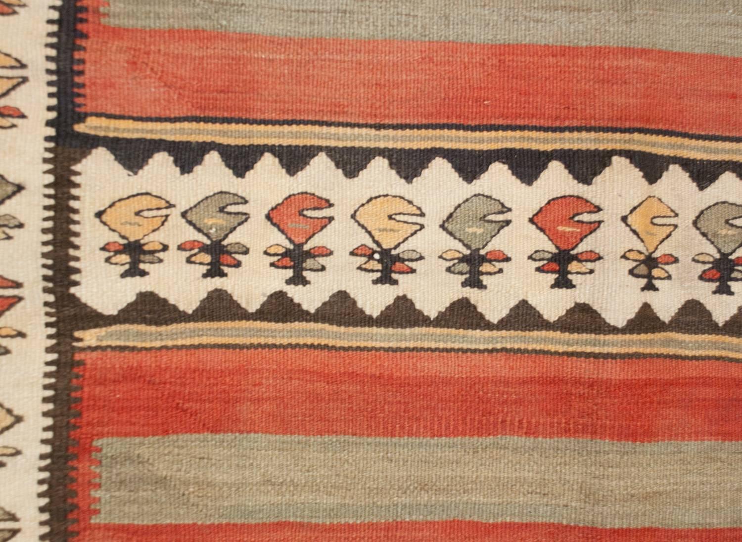 A wonderful early 20th century Persian Zarand Kilim runner with a bold pattern of alternating crimson, pale indigo, black and gold zigzag, and floral patterned stripes. The border is complementary with a similar stylized floral pattern on a white