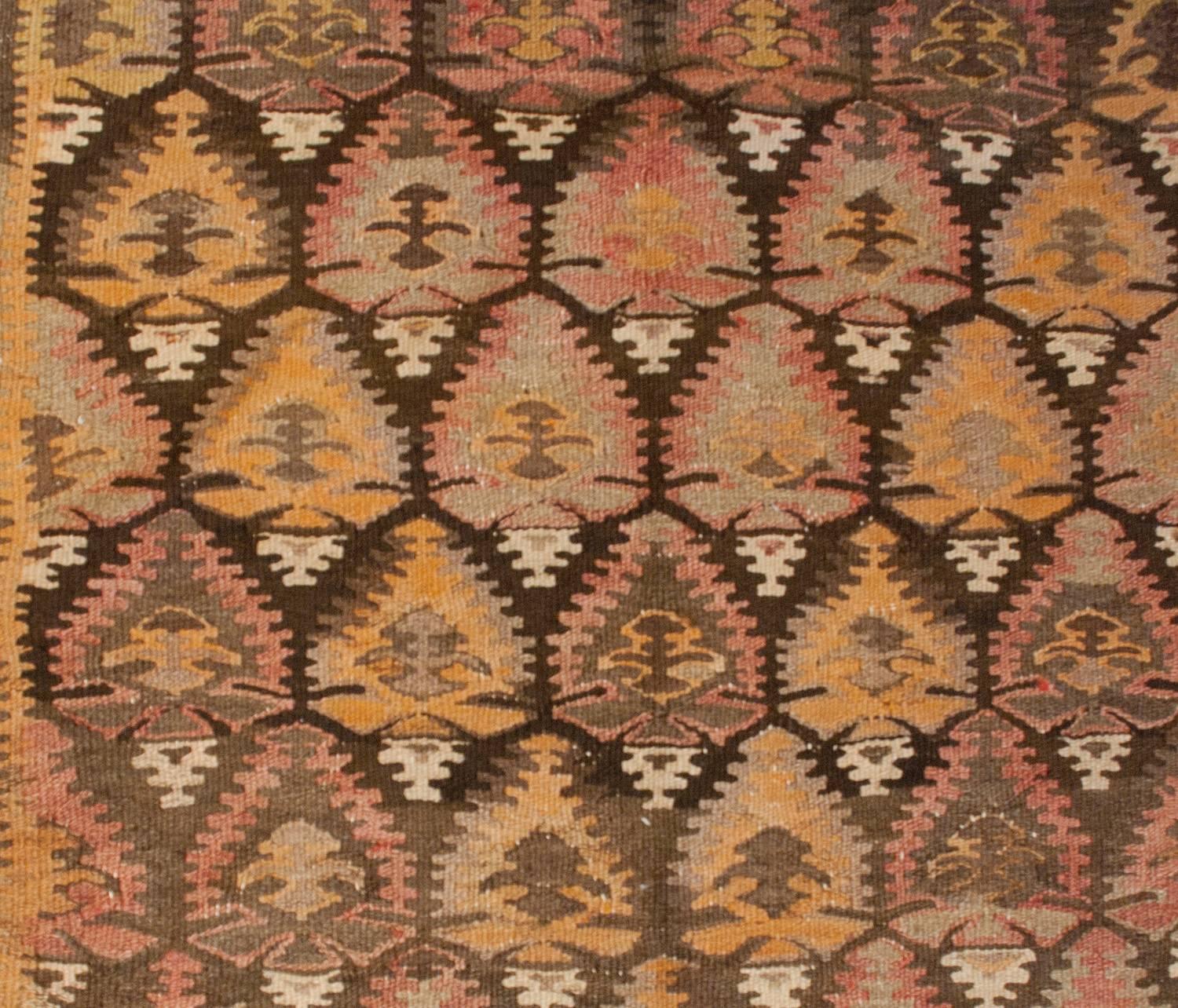 A wonderful early 20th century Persian Qazvin Kilim runner with a masterfully woven pattern of stylized tree-of-life patterns woven in brown, gold and pale red vegetable dyed wool. The border is composed of three distinct patterns. The center is a