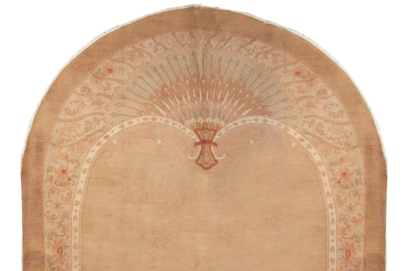 An unusual oval Chinese Art Deco rug with a fan design on each end, woven in pink, pale indigo, red and cream naturally dyed colors. The center is double-lobed kidney shape with an open field of natural color wool.