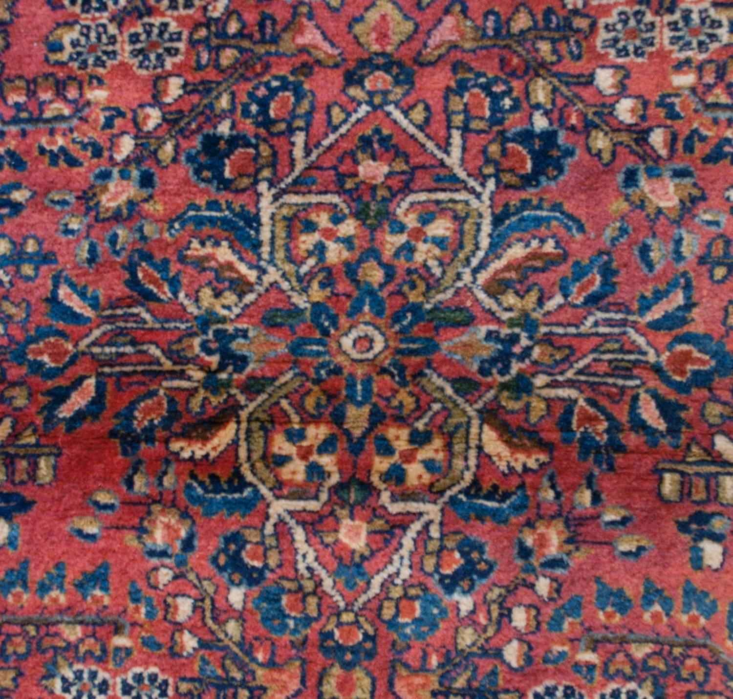 A wonderful early 20th century Persian Sarouk rug with a masterfully woven field of large trees-of-life and myriad floral varieties woven in dark and light indigo, crimson, and cream naturally dyed wool on a deep cranberry field. The border is wide