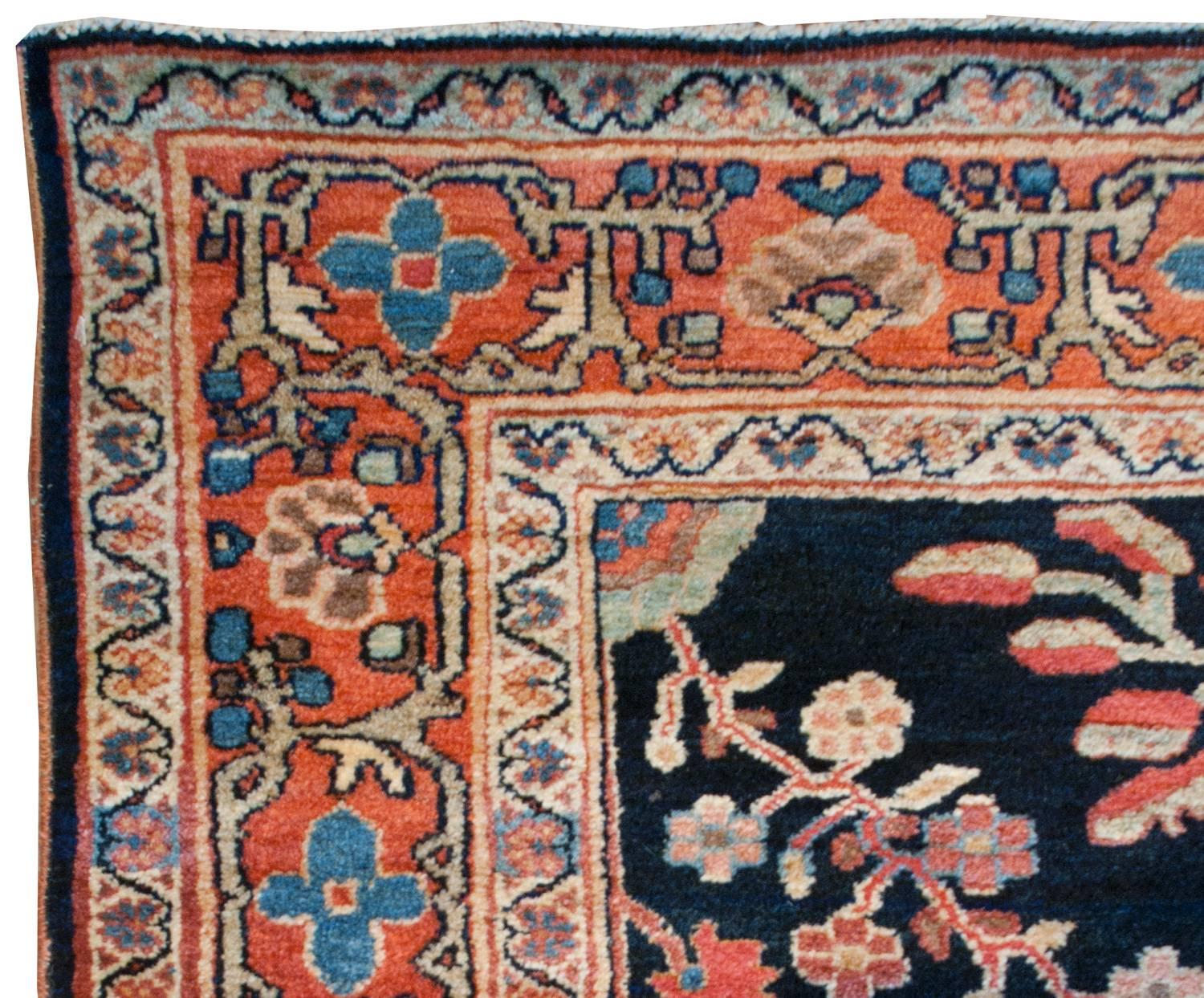 A unique early 20th century Persian Sarouk rug with an interesting English Arts & Crafts-inspired floral pattern with large multicolored, almost geometric-form, flowers on a dark indigo background. A central crimson medallion has stylized vines