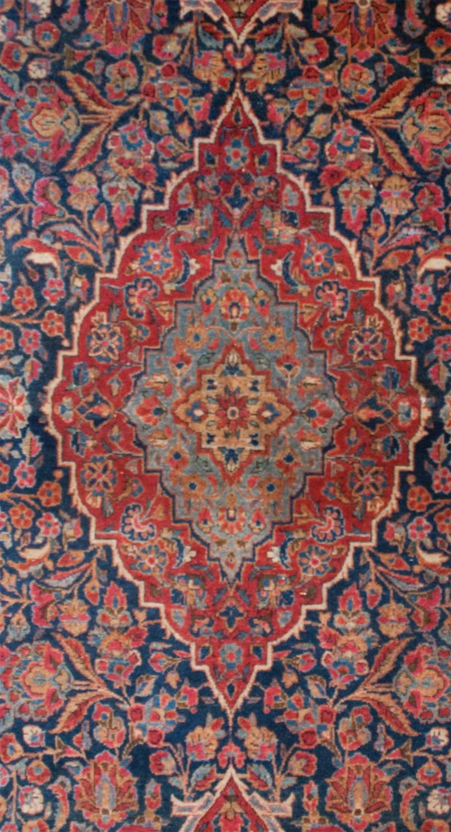 An outstanding early 20th century Persian Kashan rug with an extraordinary pattern of myriad intertwined blossoming branches woven in dark and light indigo, cranberry, crimson, and natural wools. The border is exceptional with a complementary