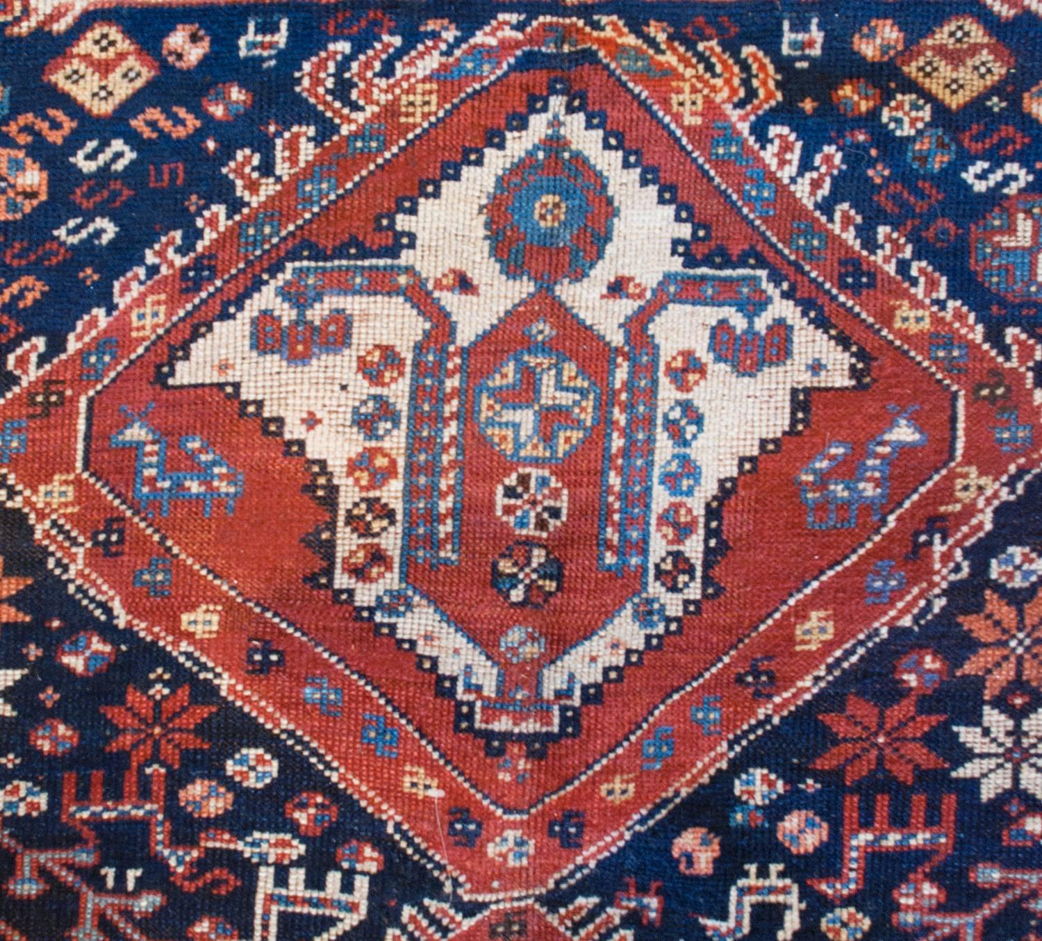 An incredible late 19th century Persian Ghashghaei rug with two large crimson and indigo diamond medallions amidst a fantastic field of flowering bushes, trees-of-life, and myriad animals including deer, birds and goats, all on a dark indigo