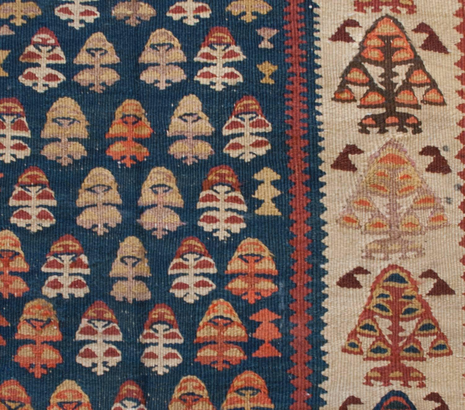 An exceptional early 20th century Kurdish Kilim runner with an amazing brilliant color pallet of crimson, coral, gold, indigo, and natural wool. The central field is wonderful with stylized trees-of-life in a brilliant indigo background. The border