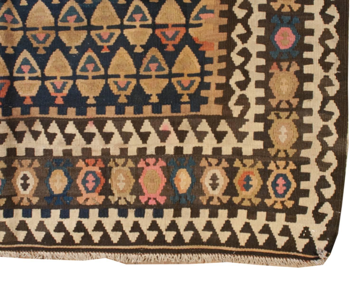 Un inhabituel chemin de table en veramin Kilim persan du début du 20e siècle avec un motif d'arbre de vie multicolore, presque géométrique, tissé de manière complexe sur un fond indigo. La bordure est audacieuse, avec des formes de vigne stylisées