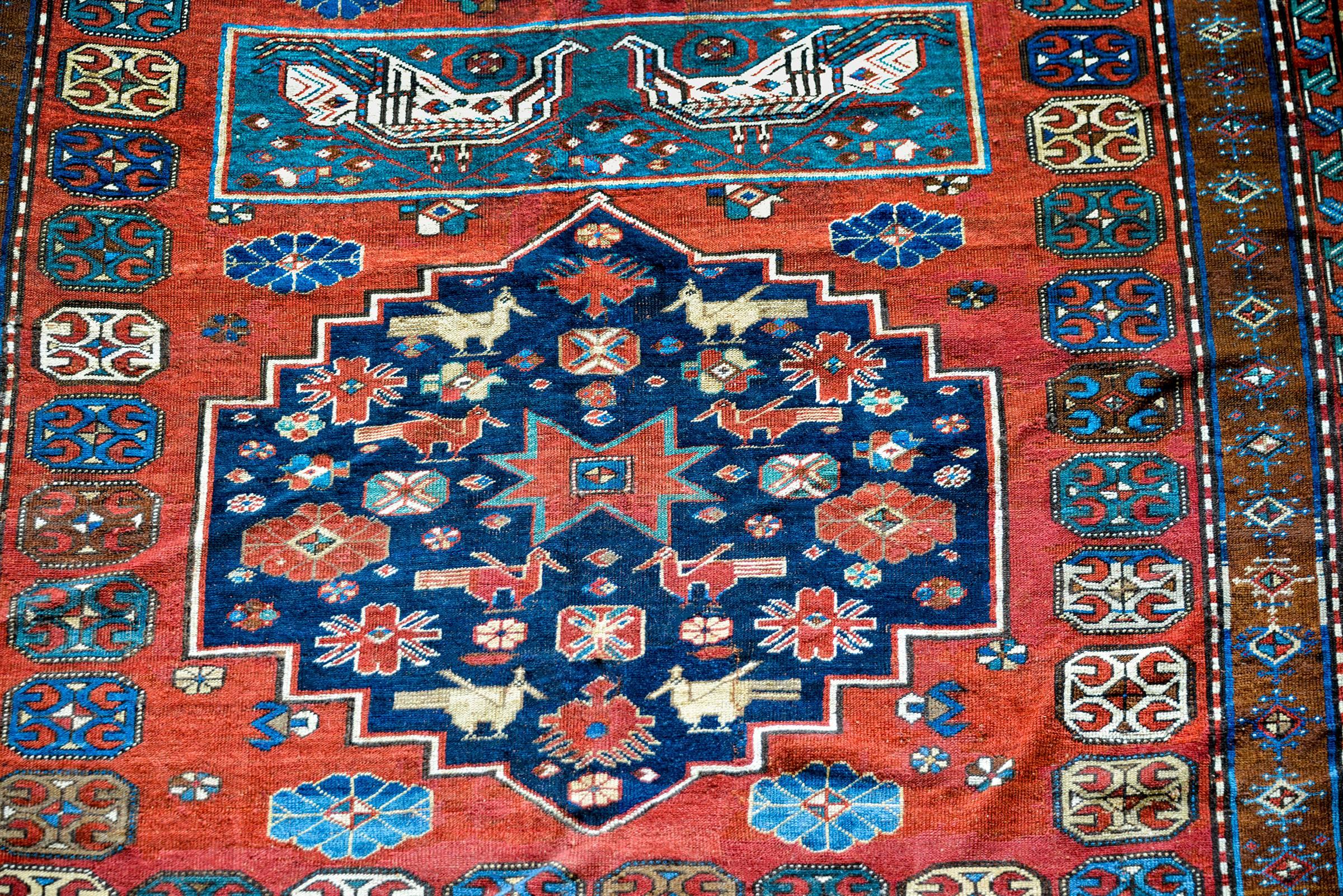 An extraordinary early 20th century Caucasian rug with a fantastically woven pattern consisting of three large diamond shaped medallions, two with dark indigo backgrounds, and one with white, with multicolored flowers and birds, on a rich deep