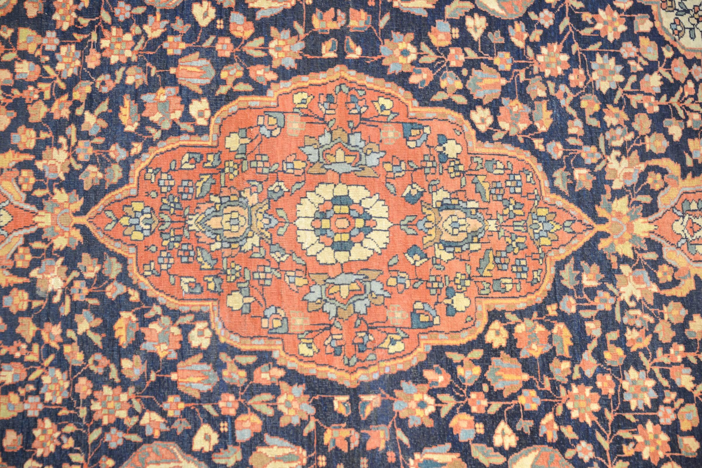 An exceptional late 19th century Persian Sarouk Farahan rug with a wonderful large crimson medallion woven with a tight floral and vine pattern, on a dark indigo field with scrolling vines and leaves. The border is wide with a complementary floral