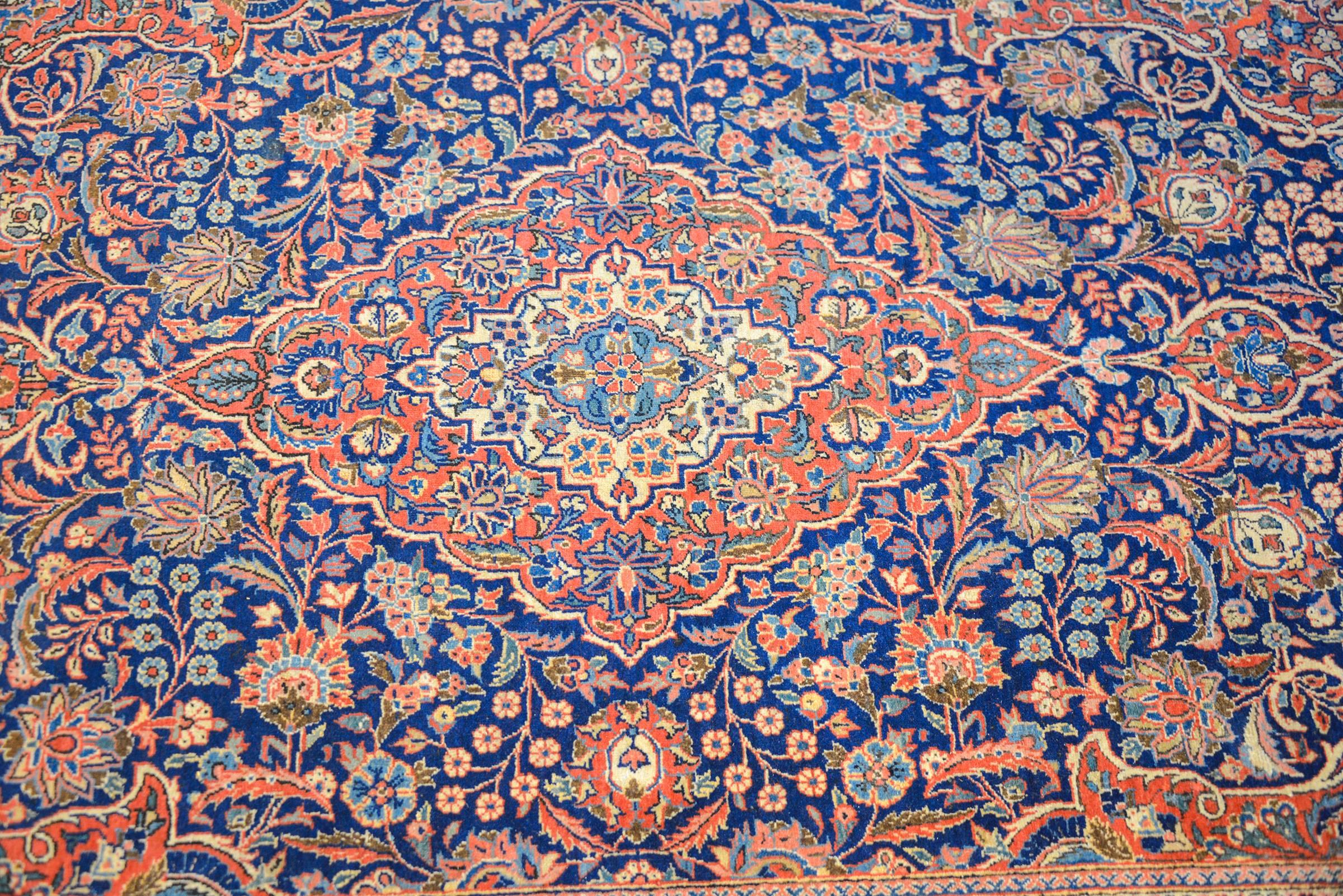 An amazing early 20th century Persian Kashan rug with an intense densely woven all-over large and small-scale floral and vine patterns rendered in crimson, indigo and natural wool colors. The border is complementary with large-scale flowers and