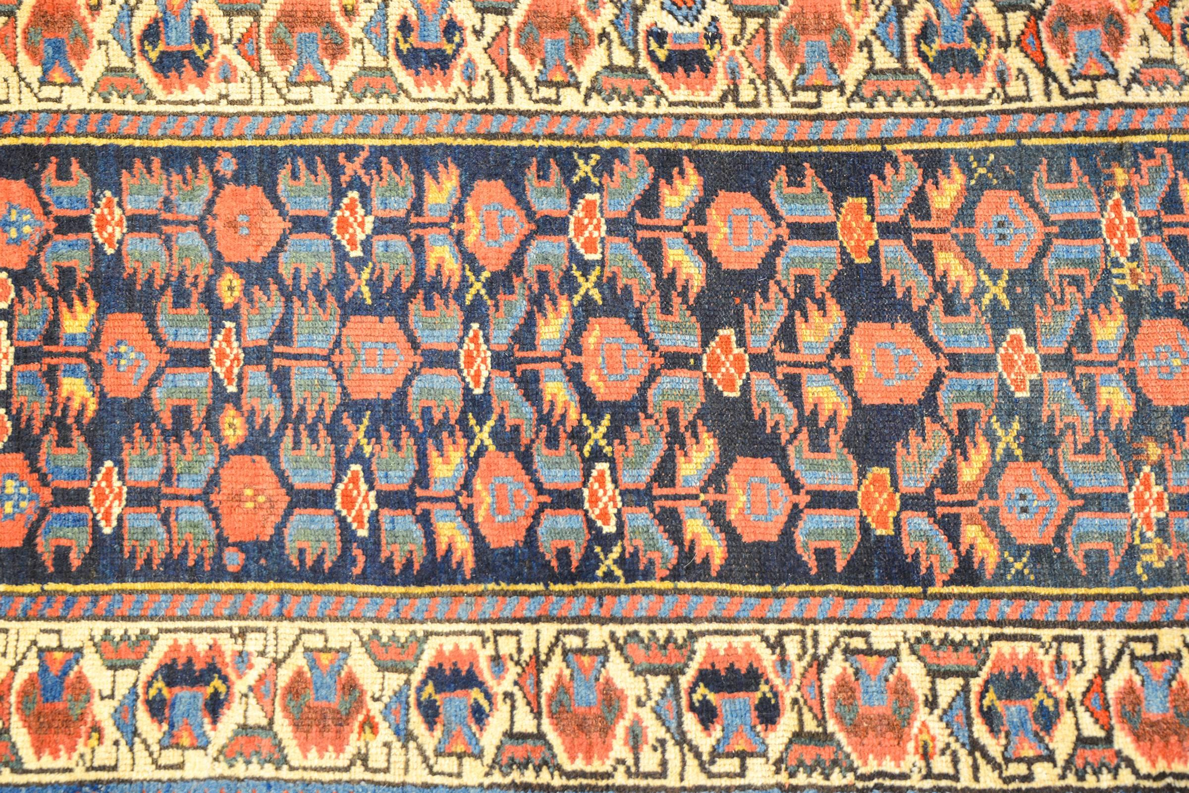 A wonderful early 20th century Persian Kurdish runner with a sweet all-over crimson and indigo floral pattern on a dark indigo background. The border is complex woven with multiple geometric and floral patterns in similar crimson and indigo colors.