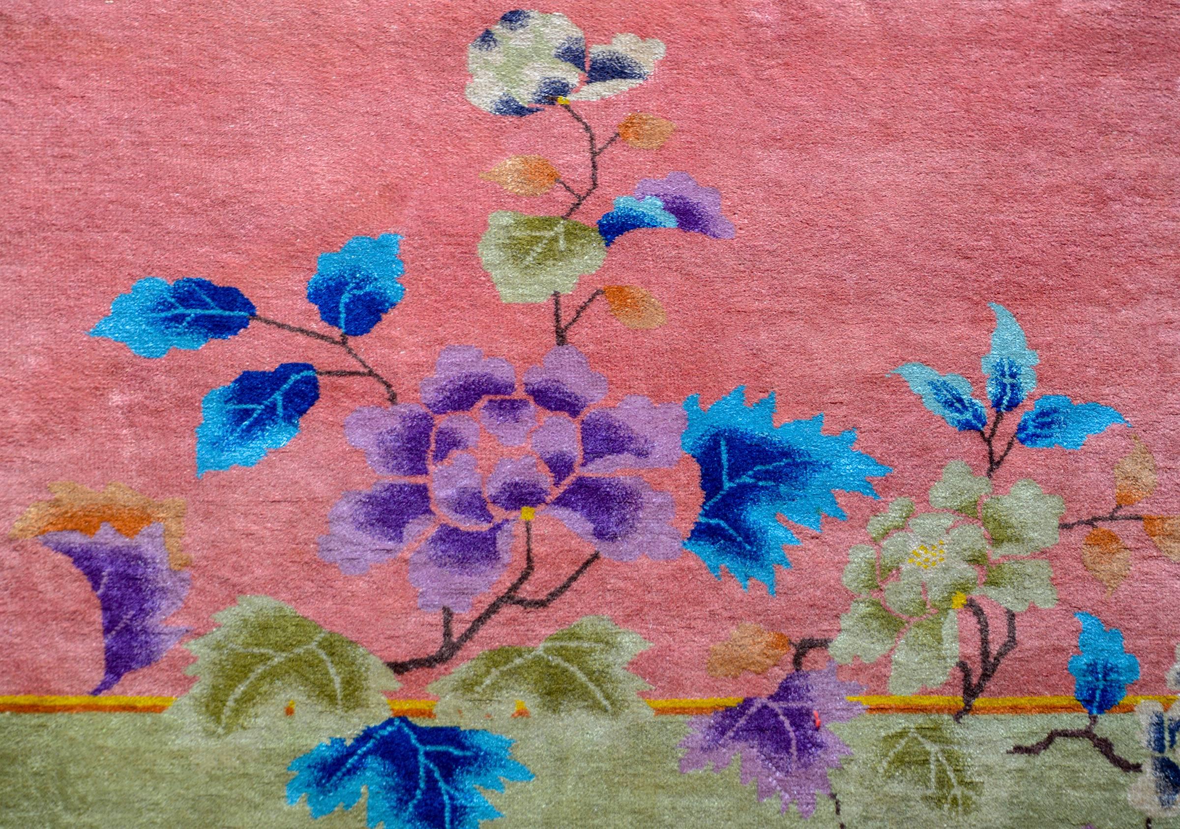 A brilliant early 20th century Chinese Art Deco rug with a sweet pink central field surrounded by a wide pea green border. An asymmetrical multicolored flowering peony and chrysanthemum and scrolling vine pattern are positioned in opposite corners.