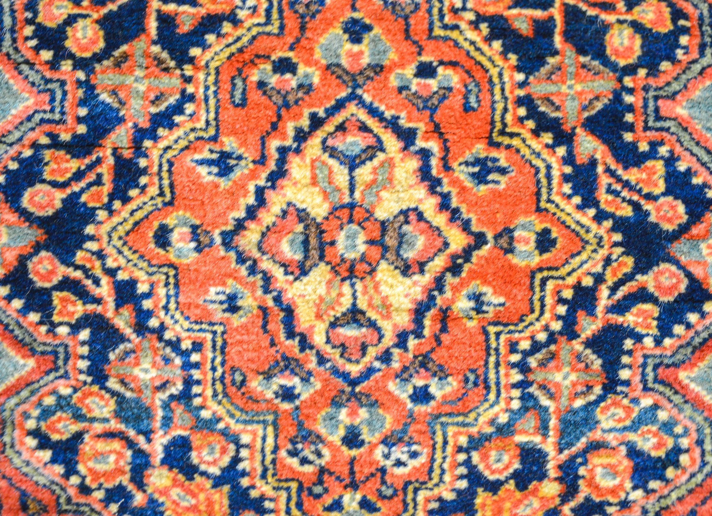 A wonderful early 20th century Persian Jozan Rug with beautiful floral and vine pattern woven in orange, cream, and green vegetable dyed wool, on a dark indigo background. The central medallion is complementary with a floral pattern. The border is