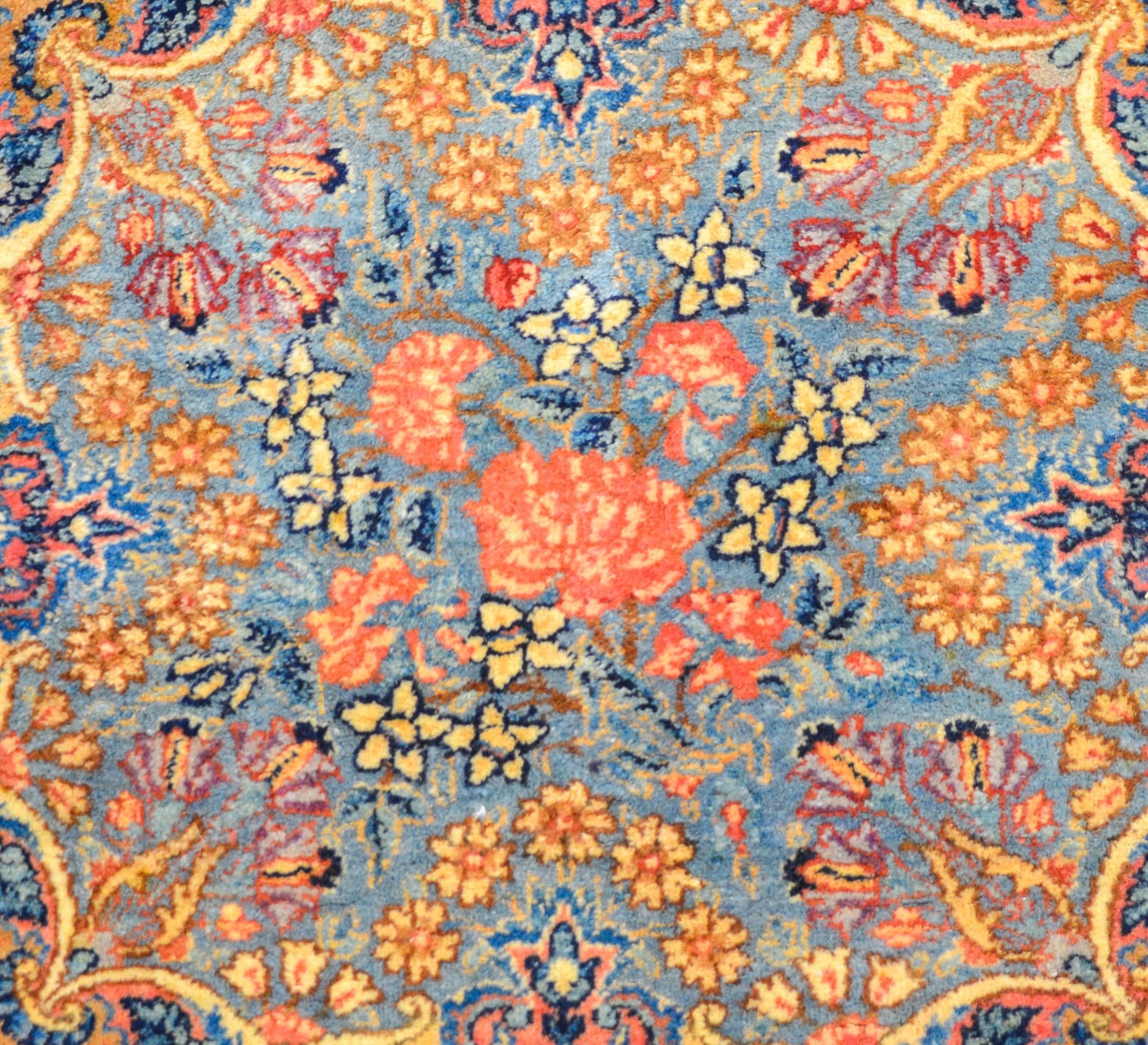 A petite early 20th century Persian Kirman mat rug with a fantastic all-over multicolored pattern depicting myriad varieties of blossoming plants. The background is pale indigo, and the flowers are woven in pink, yellow, green, indigo and violet.