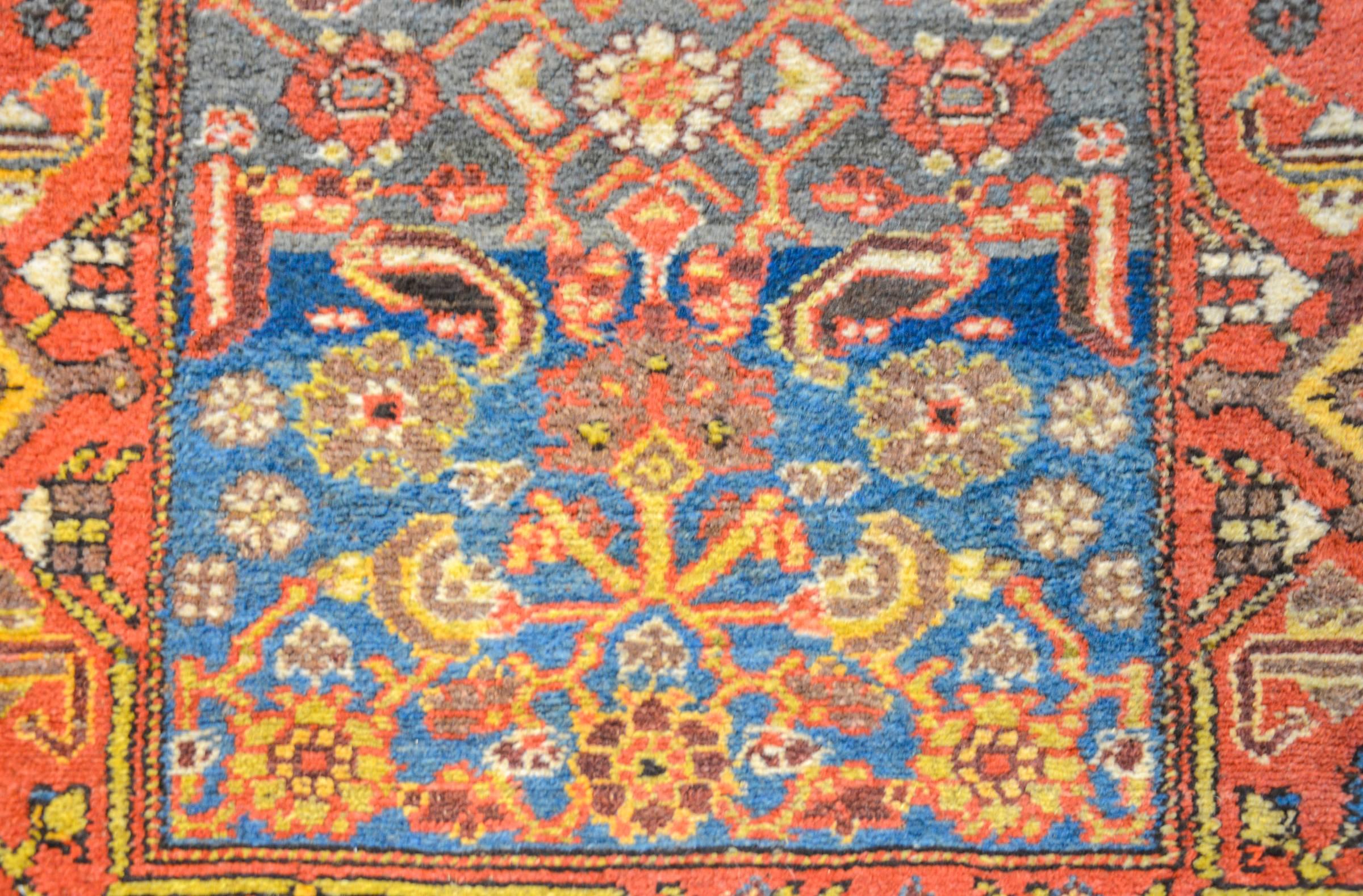 A stunning early 20th century Persian Kurdish rug with a plush pile and a striking indigo abrash field woven with an all-over gold, orange, and crimson floral and paisley pattern. The border is wide with an exceptional geometric and stylized vine