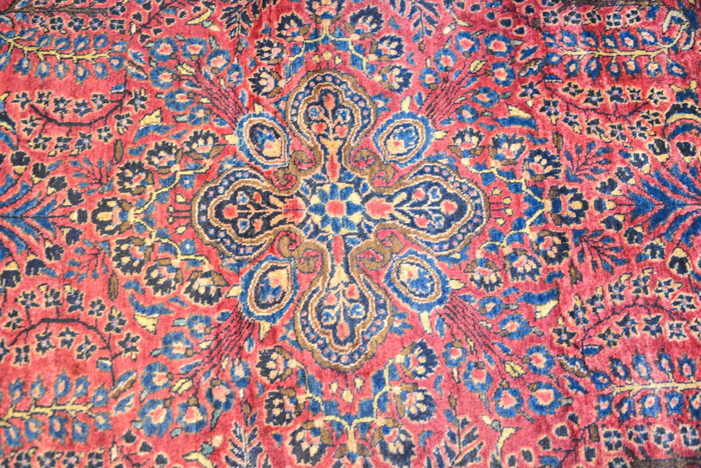 A wonderful early 20th century Persian Sarouk Maharajan rug with an exquisite all-over mirrored floral and tree-of-life pattern woven in multicolored vegetable dyed wool on a cranberry background. The border is complex with multiple wide and narrow