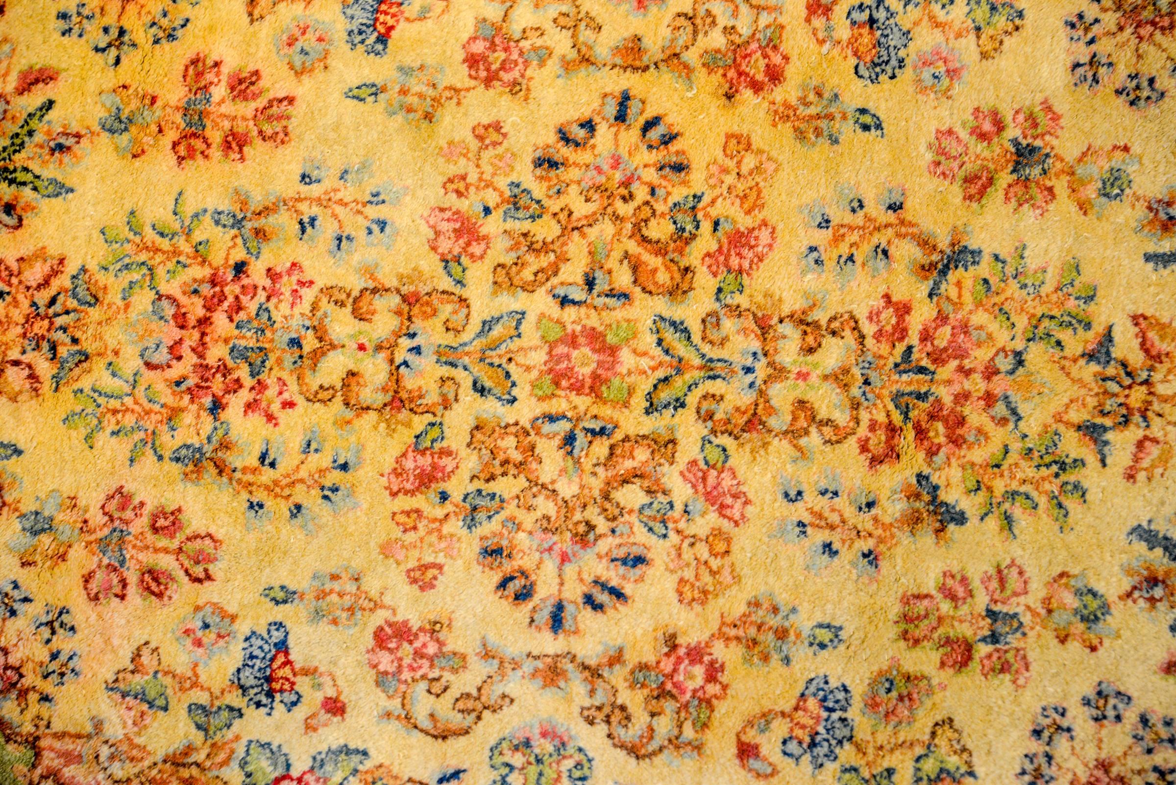 A sweet early 20th century Persian Kirman rug with a wonderful gold background with a multicolored floral and vine overplayed pattern woven in natural vegetable dyed wool. The border is unique with myriad scrolls and curved shapes woven in