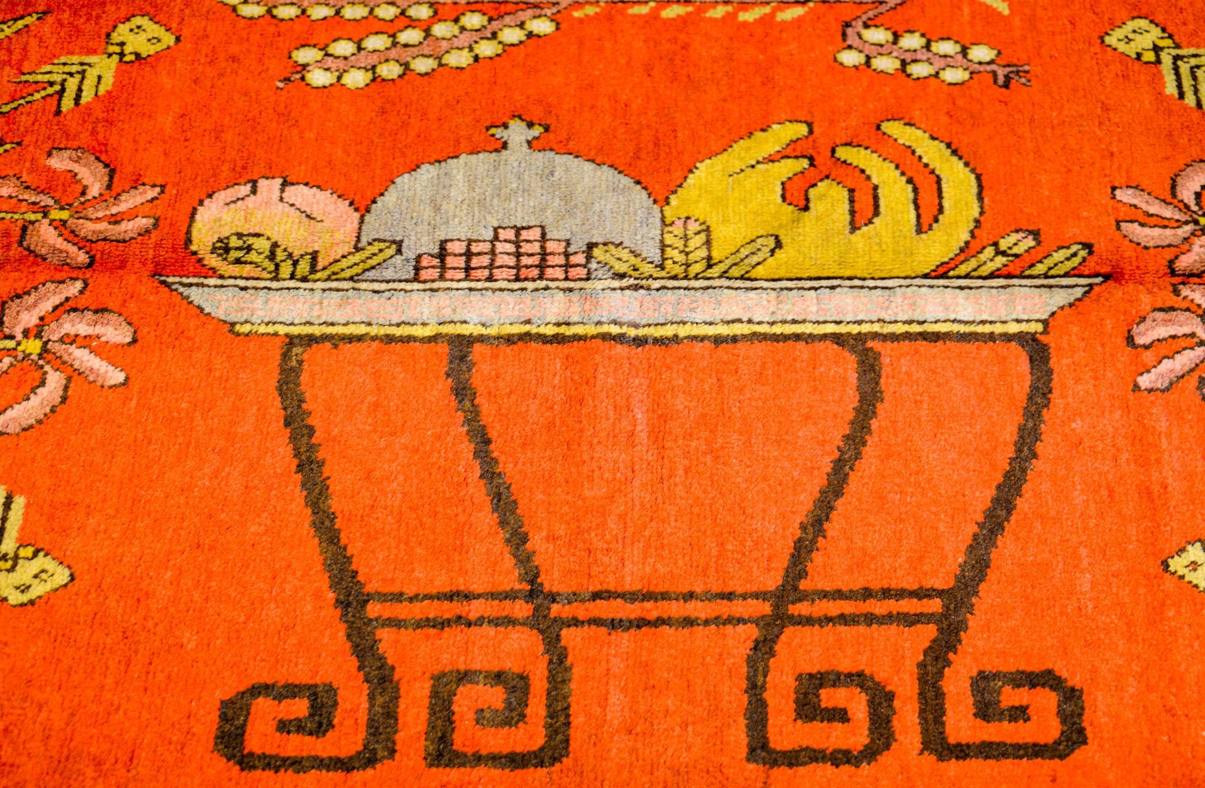 An incredible early 20th century Central Asian Khotan rug with wonderfully rendered auspicious Chinese symbols like a footed tray holding a peach, pomegranate, and citron, flanked by two blossoming lotus plants. The border is complex with multiple