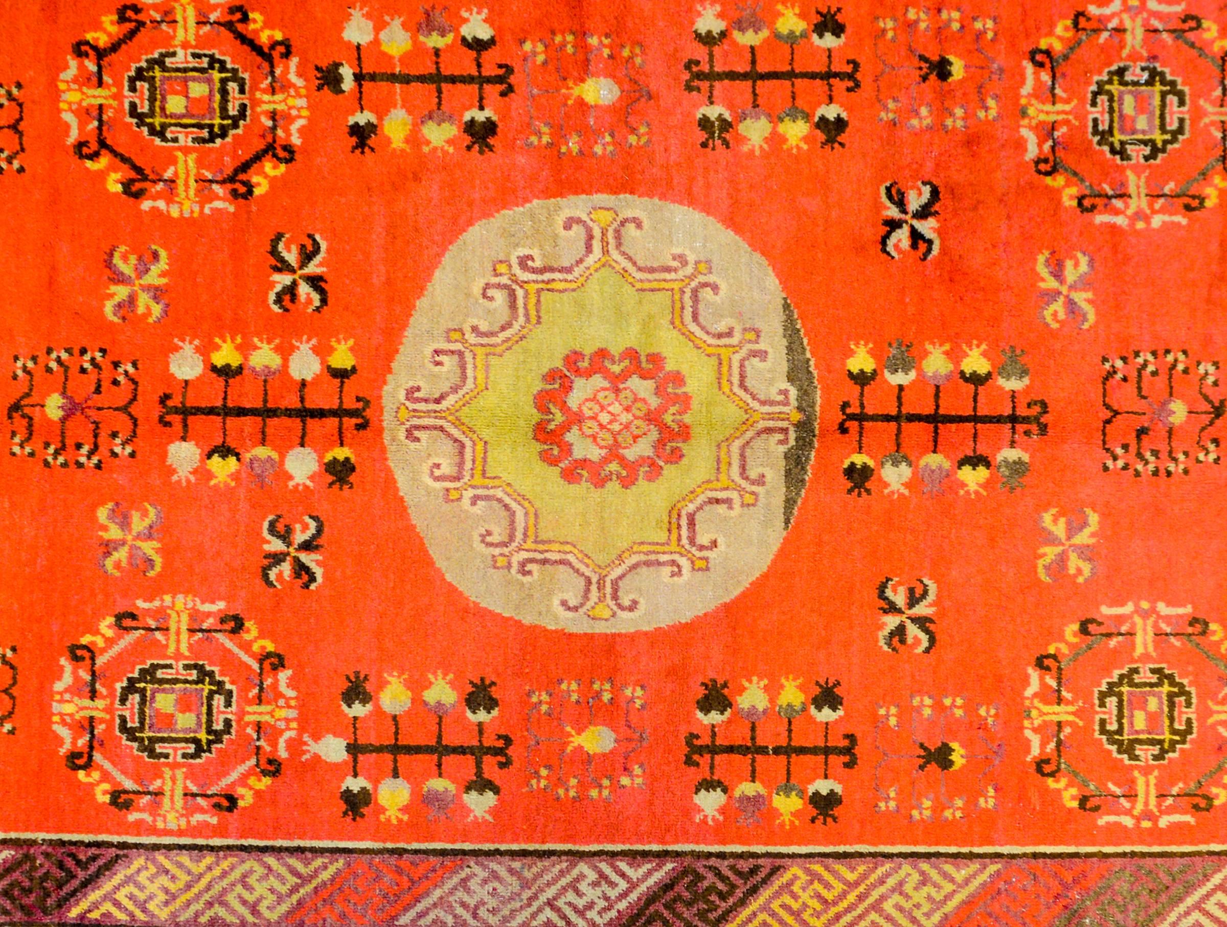 An amazing early 20th century Central Asian Khotan rug with a wonderful burnt red or orange abrash background with a large central pale indigo medallion surrounded by a field of tree-of-life and pomegranate motifs. The border is exquisite, with an